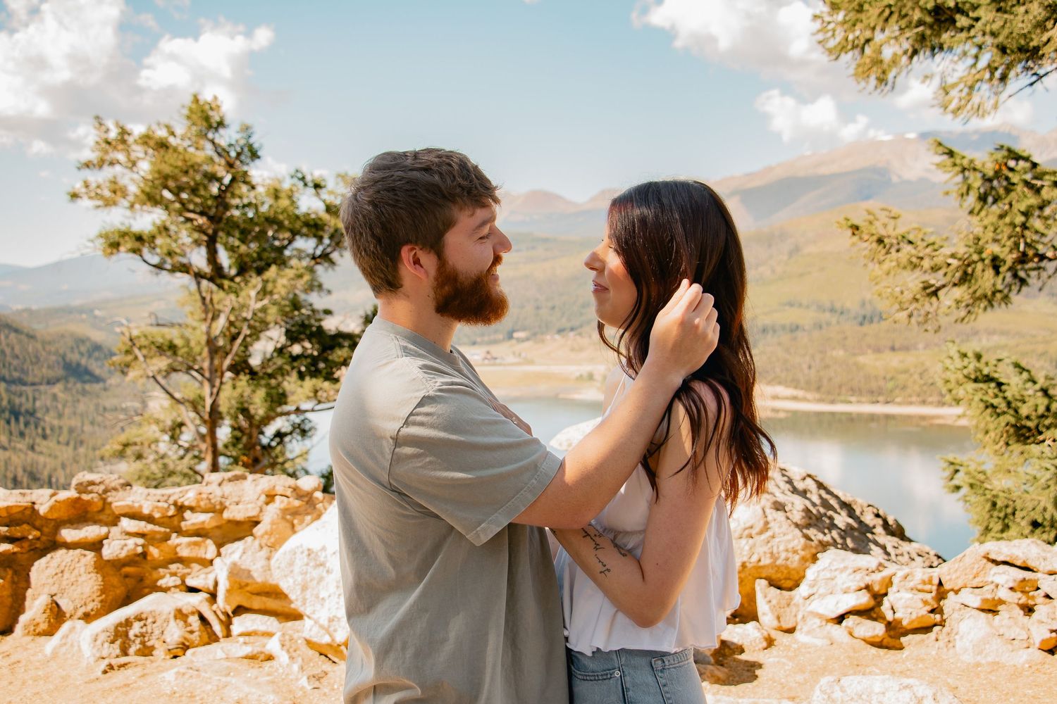 A couple embraces during a mountaintop photography session with sweeping mountain vistas in the background at sunset.