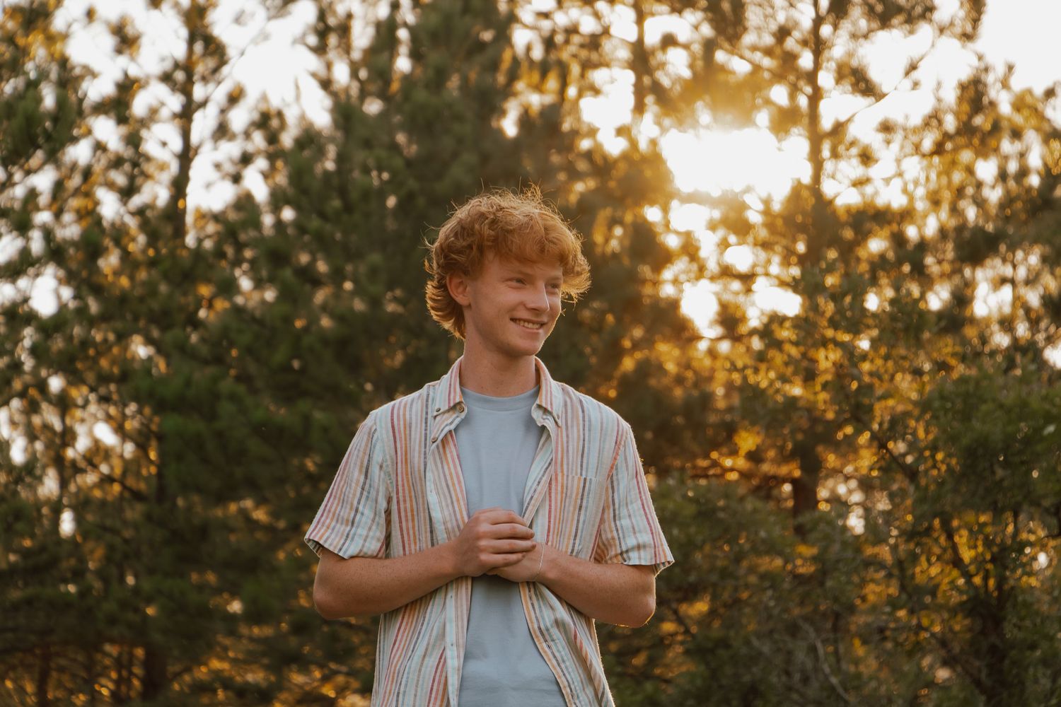 Young person in blue shirt enjoys sunset in golden light during autumn outdoor photoshoot.