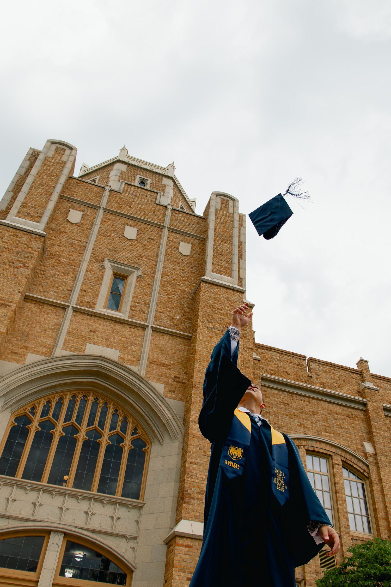 Blue graduation cap being tossed in the air against a brick collegiate building with gothic architecture.