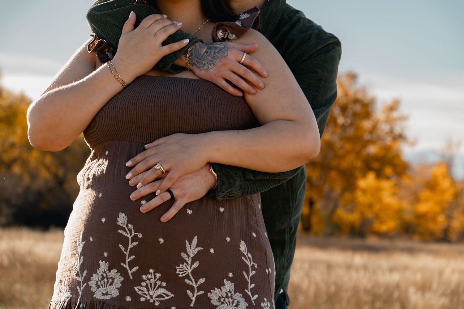 Romantic couple embraces in a sunlit autumn field with golden foliage in the background.