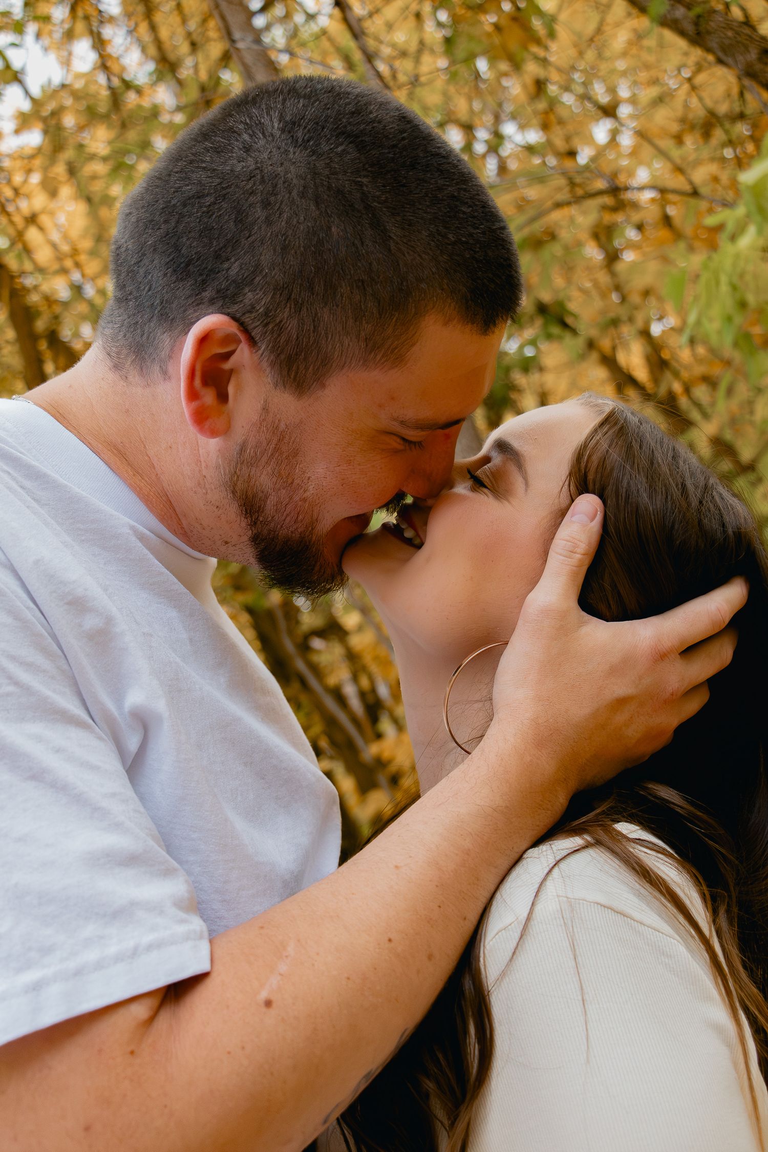 A romantic couple shares an intimate moment together outdoors during autumn with golden leaves in the background.