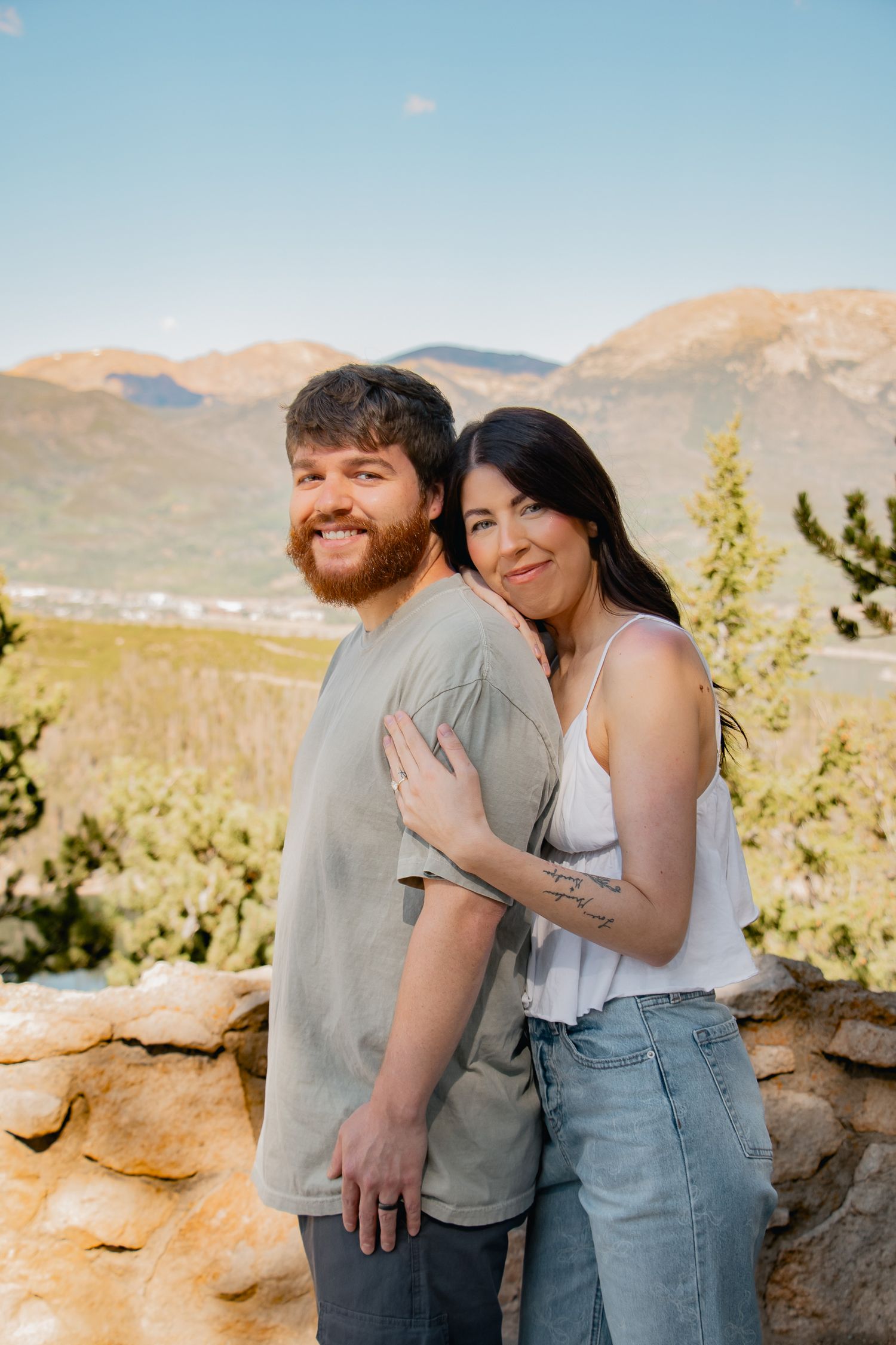 A couple embraces and laughs together during a mountain engagement photo session in a scenic rocky landscape.