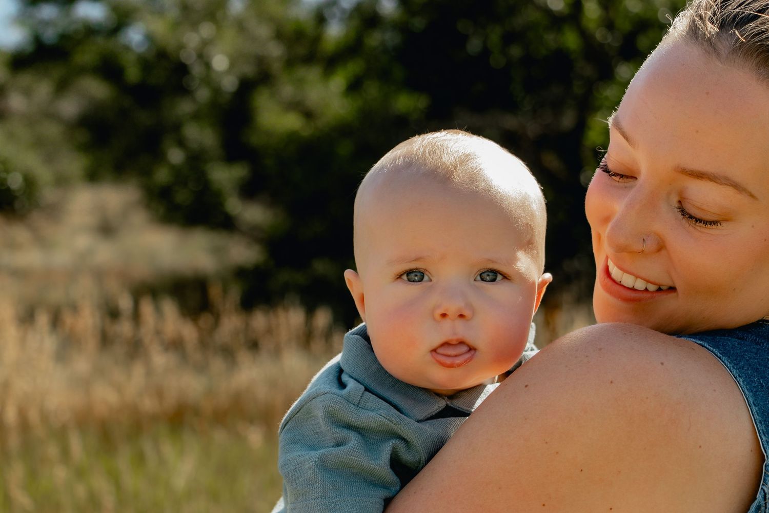 Parent and baby enjoying a tender moment together outdoors in golden sunlight against a natural background.