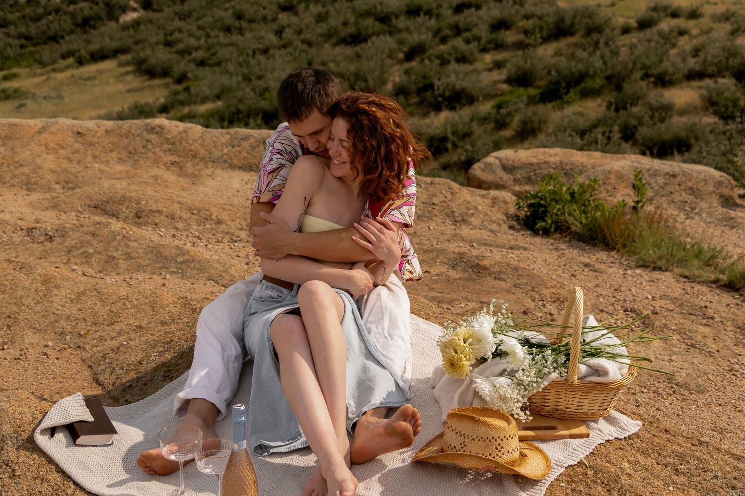 A romantic hillside picnic setup with a blanket and woven basket against a golden natural landscape.