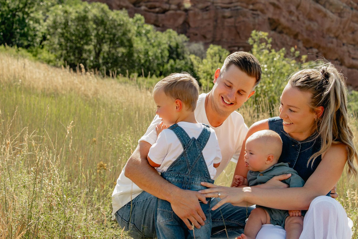 A family relaxes together in a sunny meadow with tall grass and greenery on a summer afternoon.
