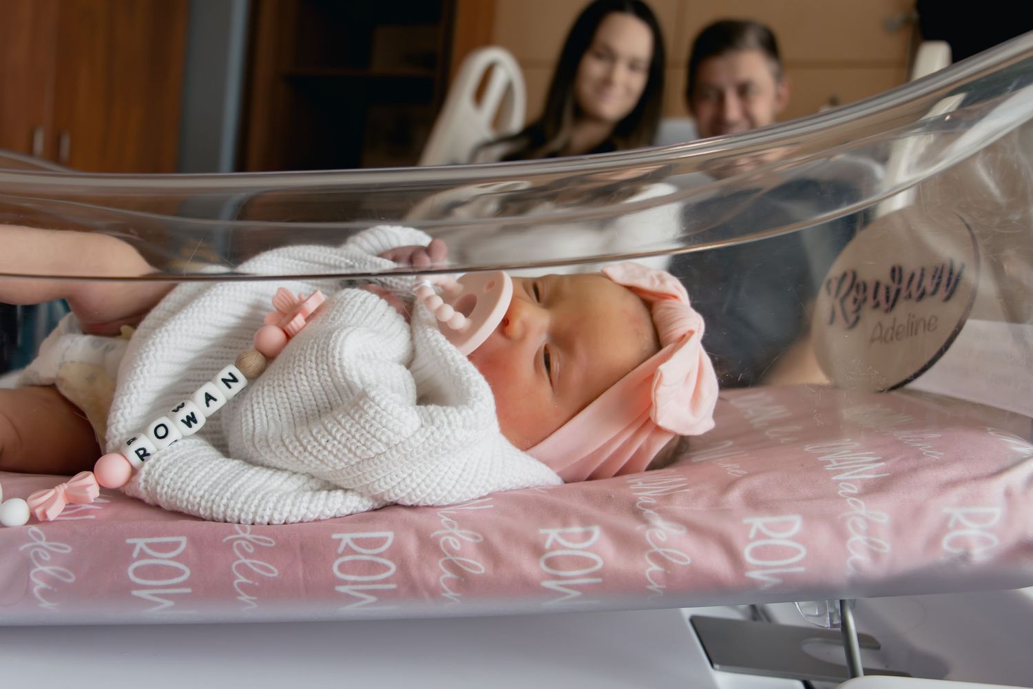 A close-up view of a premature baby's tiny hand being held in a neonatal intensive care unit.