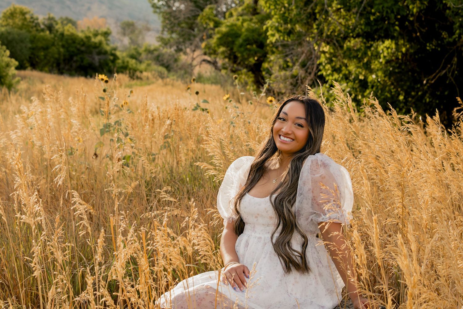 Golden summer field with someone in a flowing white dress and puffed sleeves sitting among tall wheat grass.