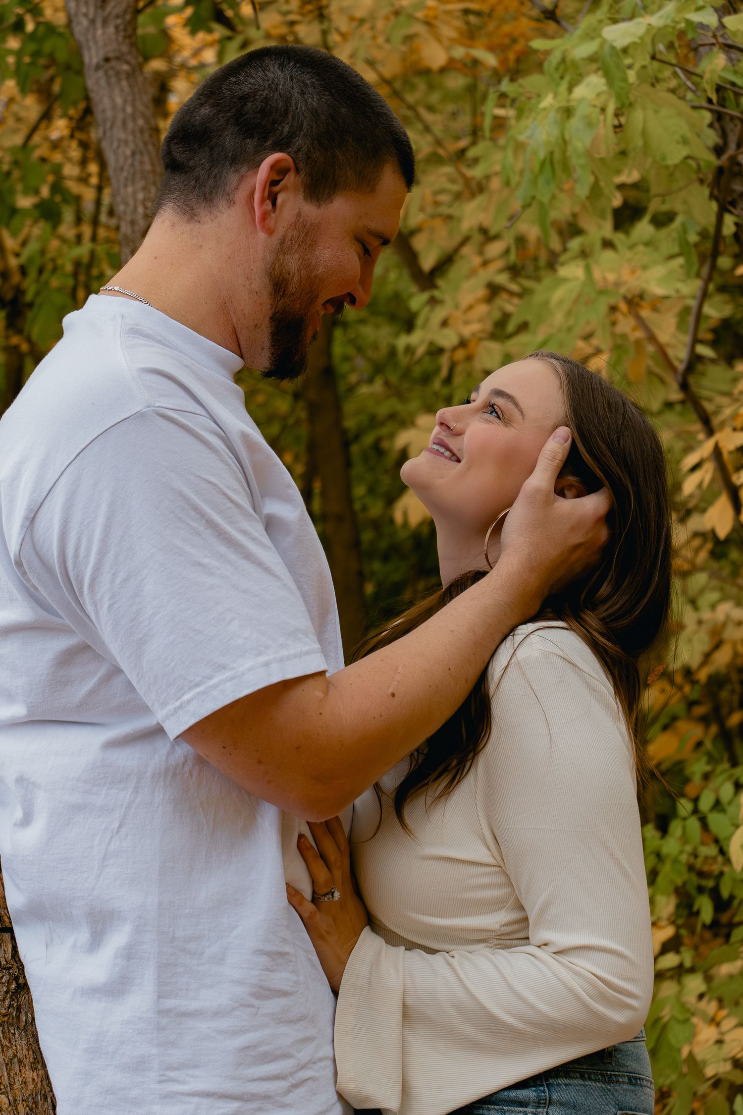 Romantic autumn engagement photo series showing tender moments between couple in white and cream against fall foliage.