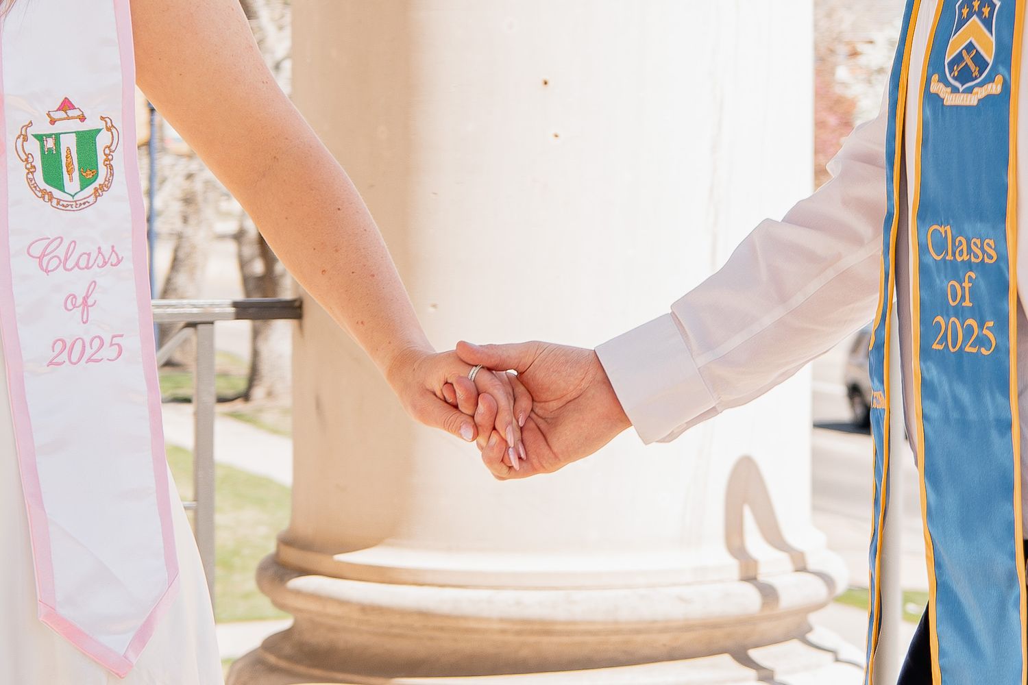 A close-up of two people holding hands during a wedding ceremony, with formal white and blue attire visible.