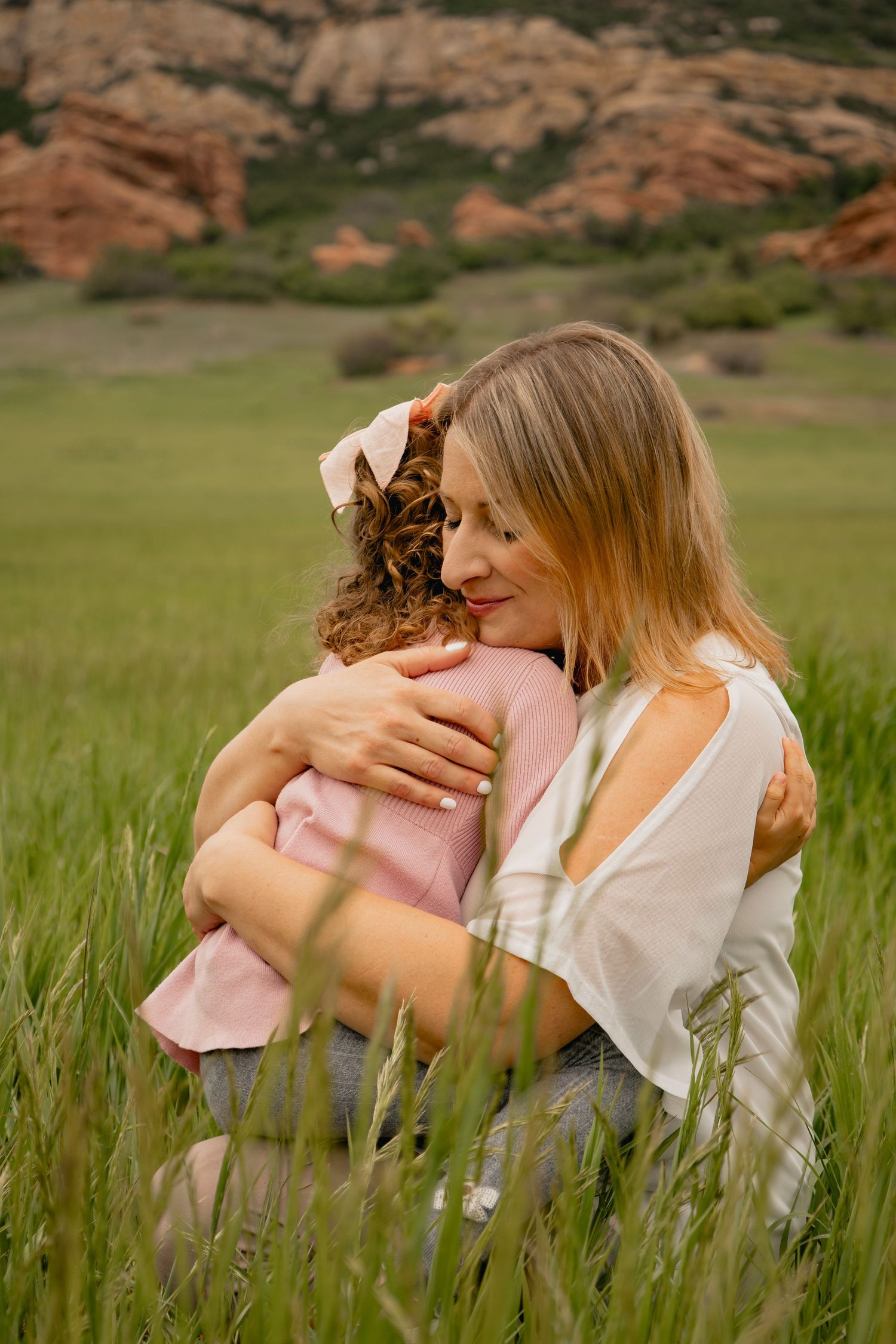 A tender embrace shared between two people in a grassy field with red rock formations in the background.