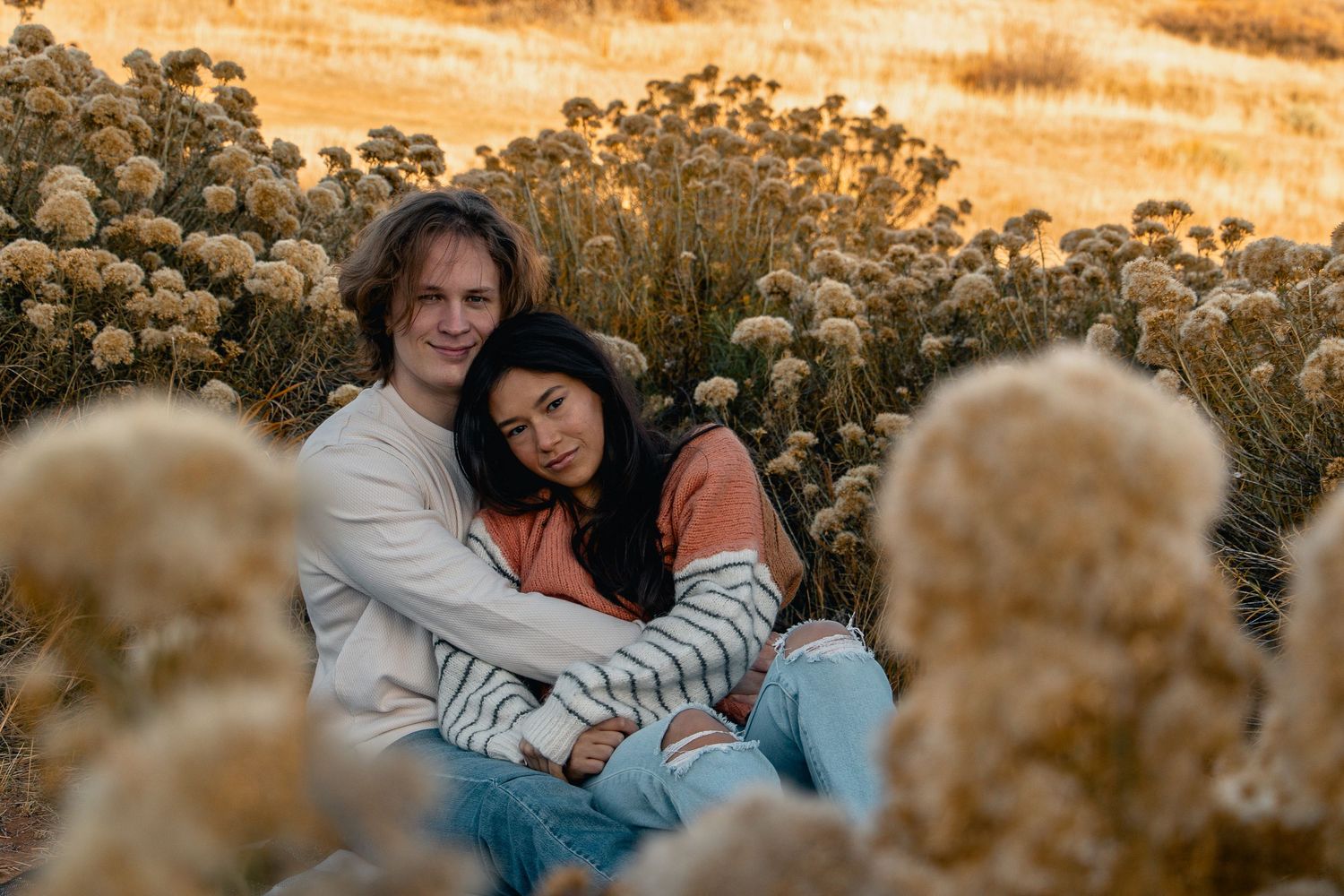 Couple cuddling together on rocky terrain during golden hour sunset.