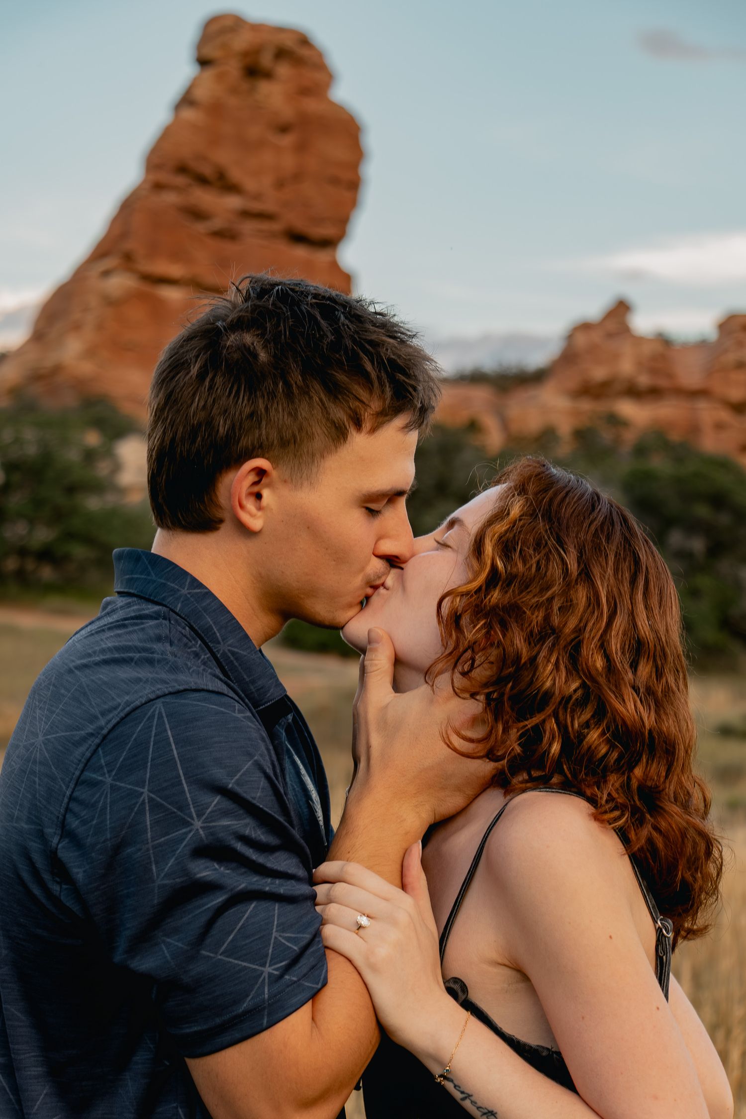 A romantic couple shares tender kisses against a backdrop of red rock formations in the desert landscape.