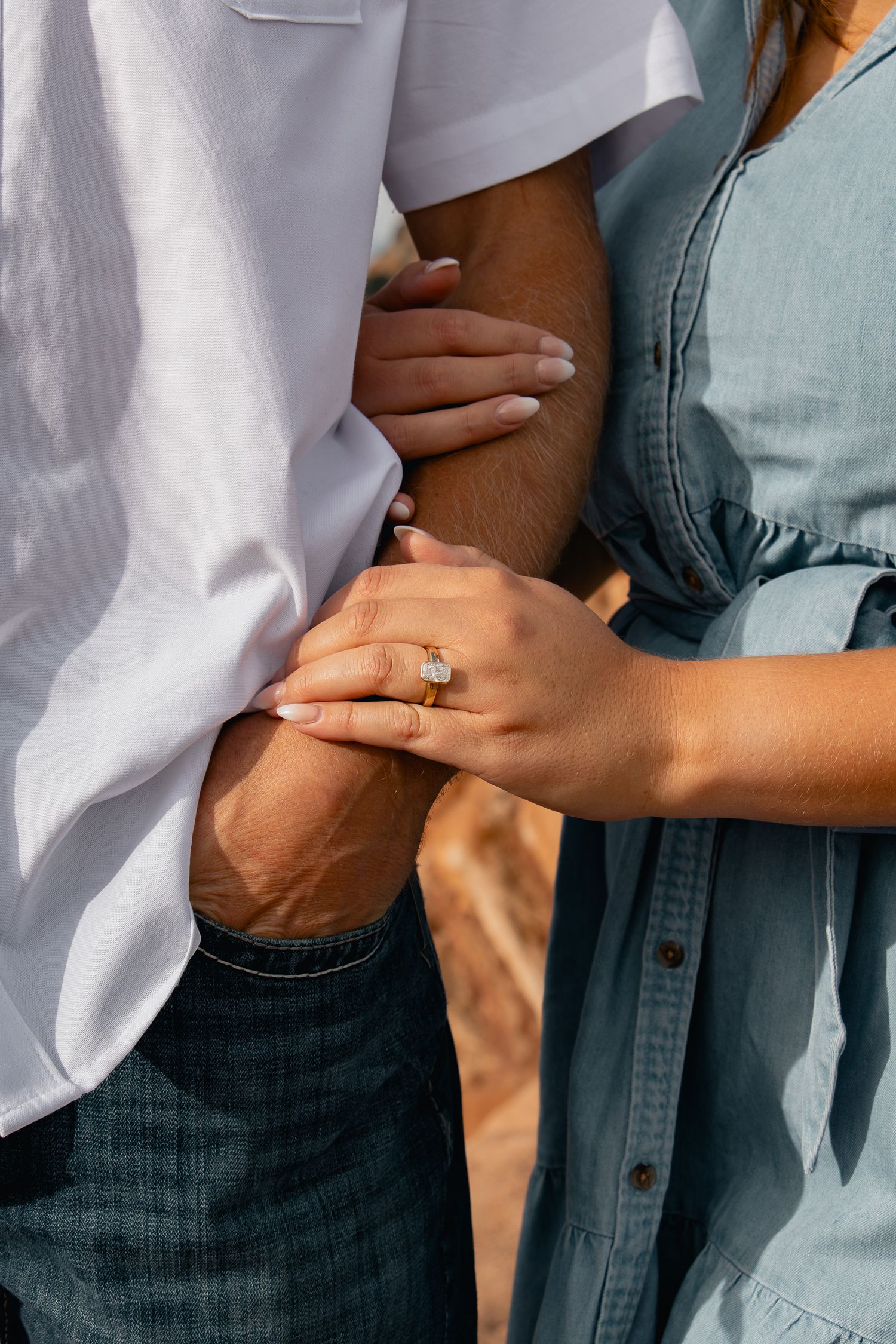 Close up of hands with engagement ring embracing against white and blue clothing.