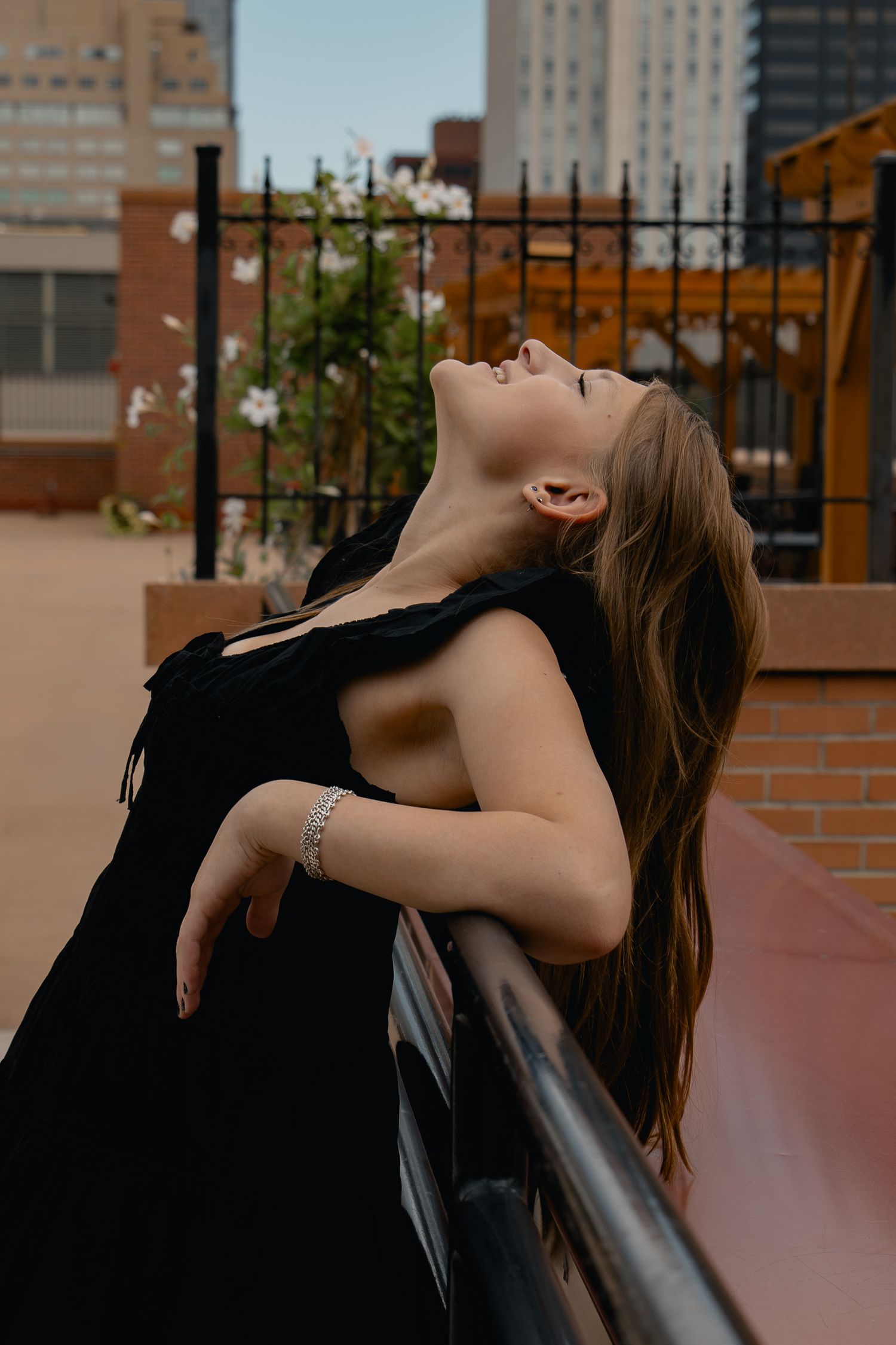 A person in black clothing leans back on a chair in an artistic series of poses against an urban backdrop.