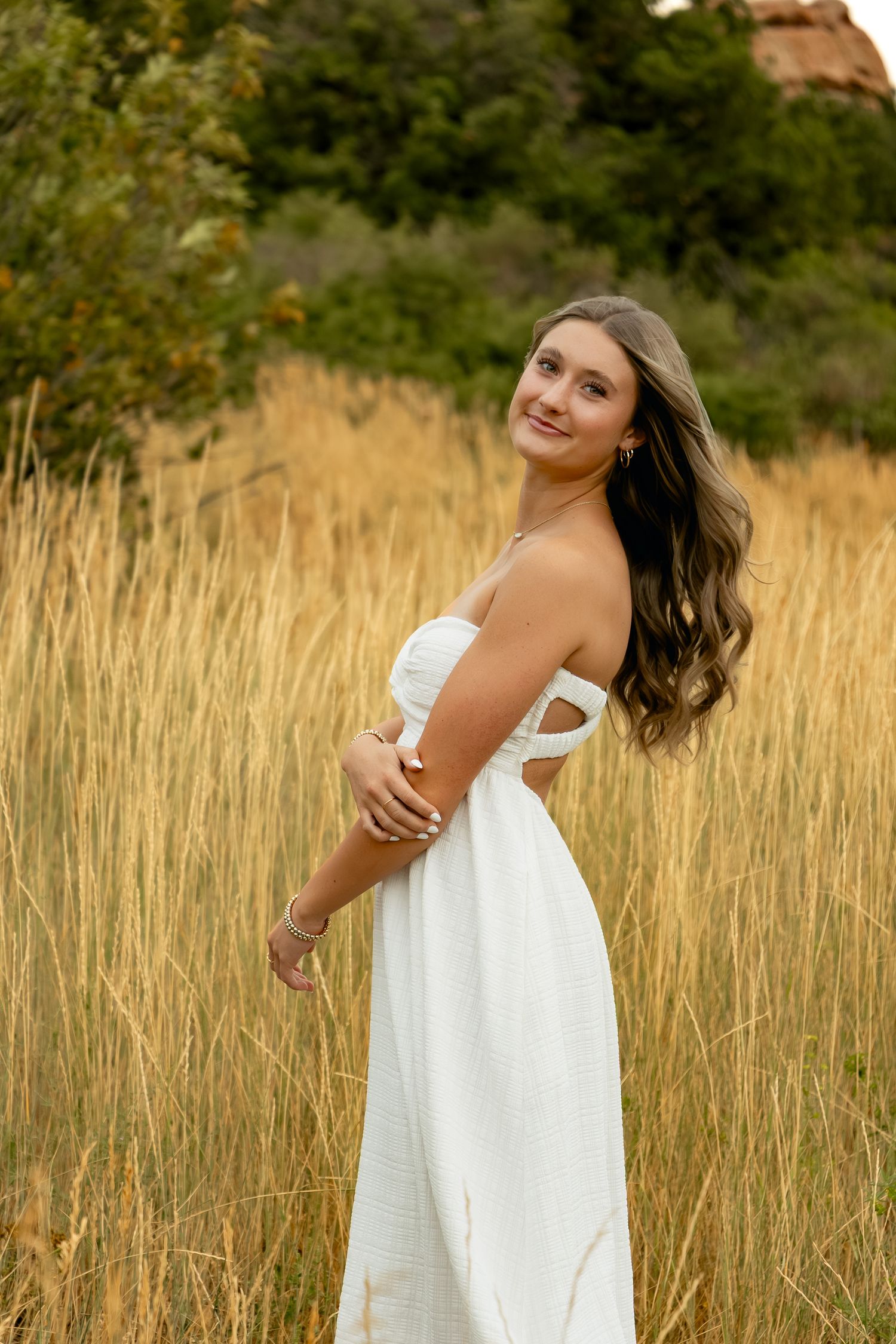 Young woman in white dress poses joyfully in tall autumn grass during golden hour outdoor portrait session.