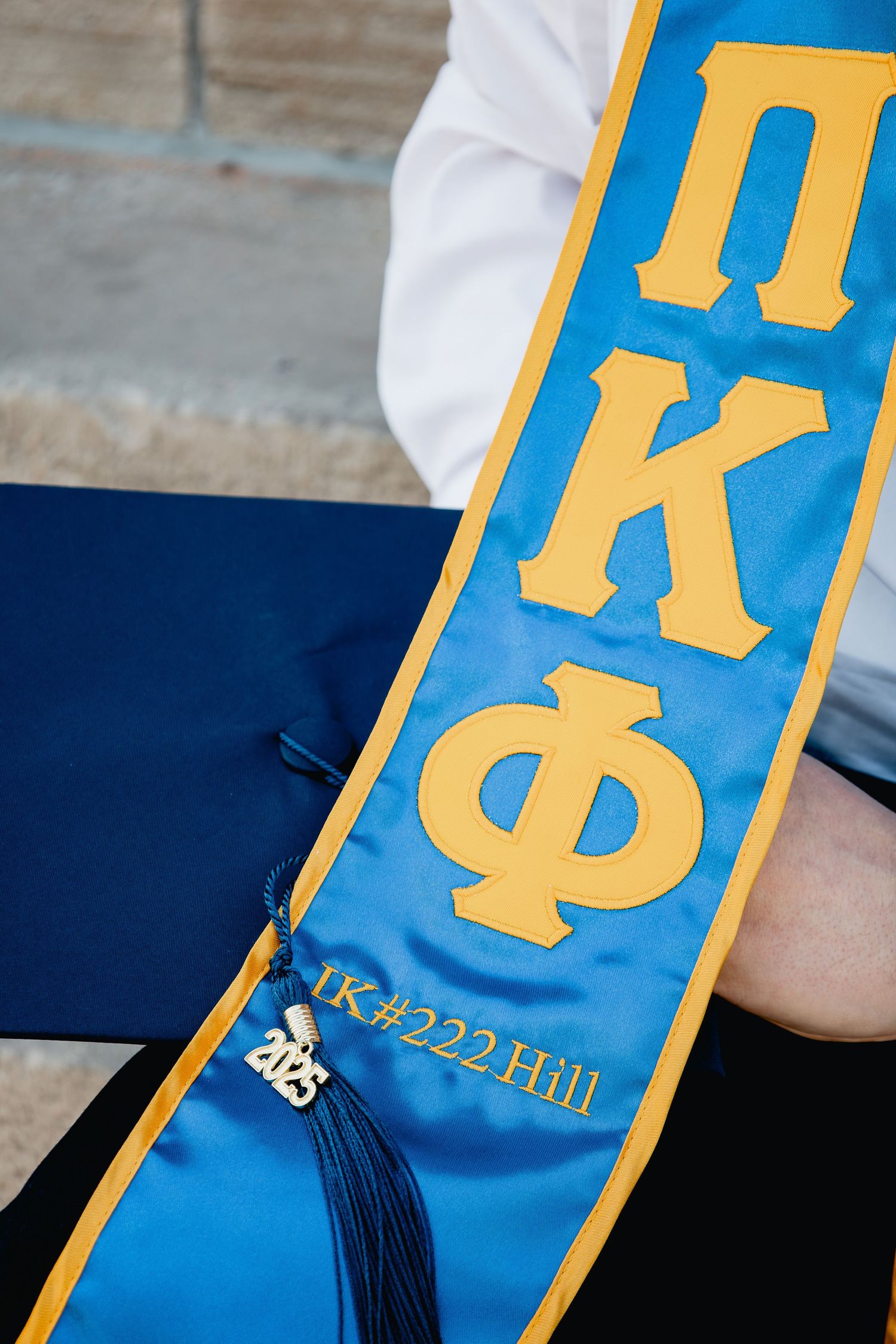 A blue and gold graduation sash for Pi Kappa Phi fraternity with '2023' and Greek letters displayed.