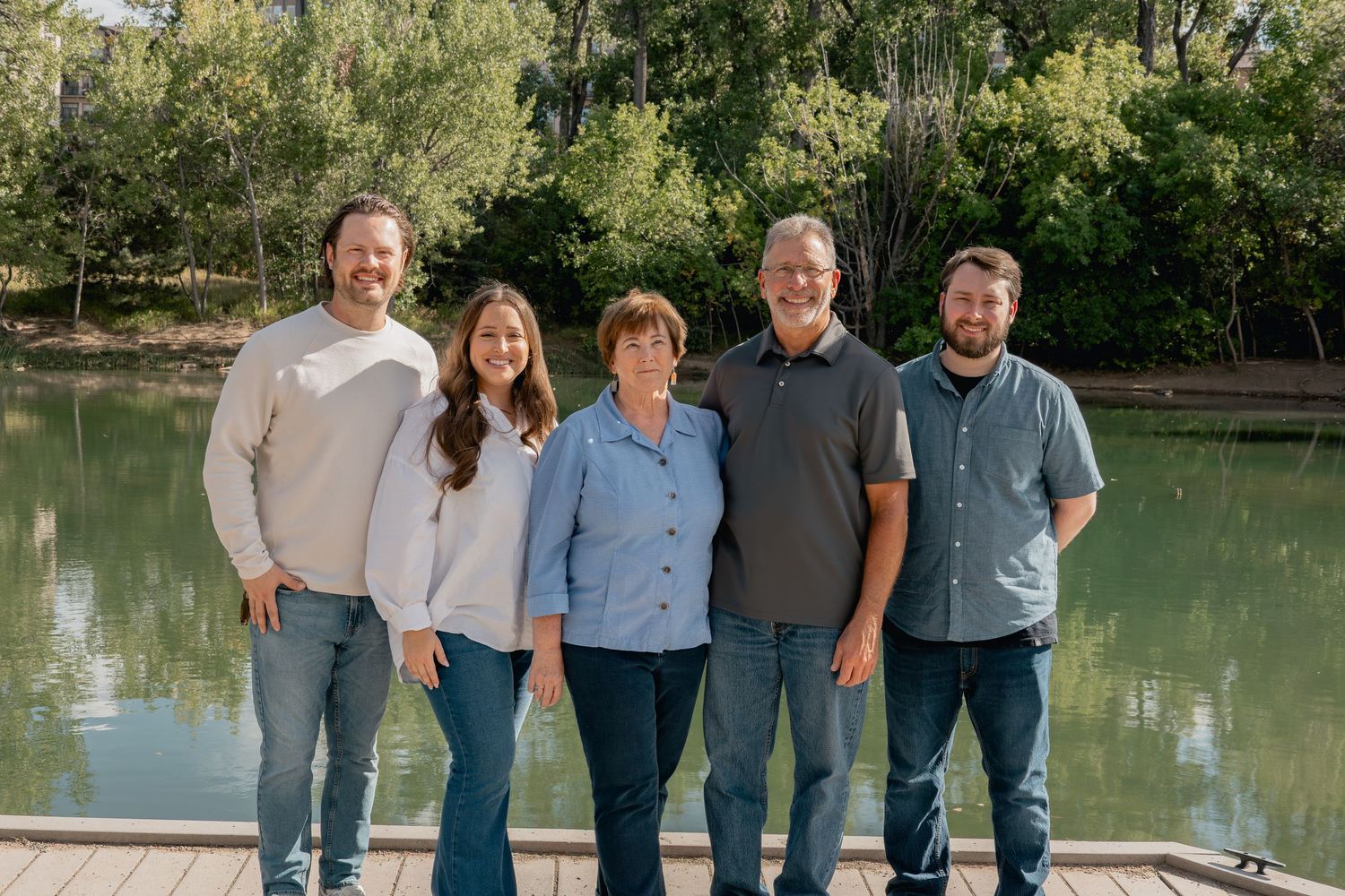 A group stands together by a peaceful lake surrounded by trees in a scenic outdoor setting.
