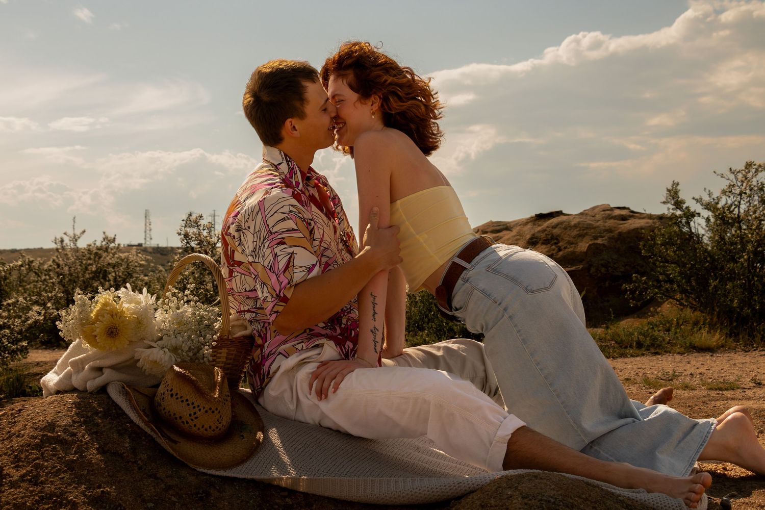 A romantic couple sits against a beautiful sunset backdrop in a peaceful countryside setting.