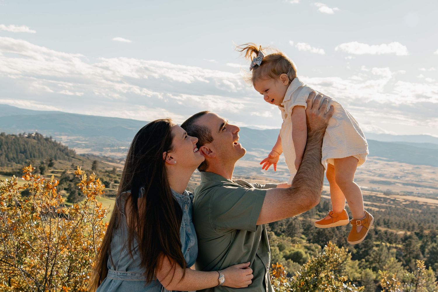 A couple shares tender moments with their child against scenic mountain landscapes at sunset.