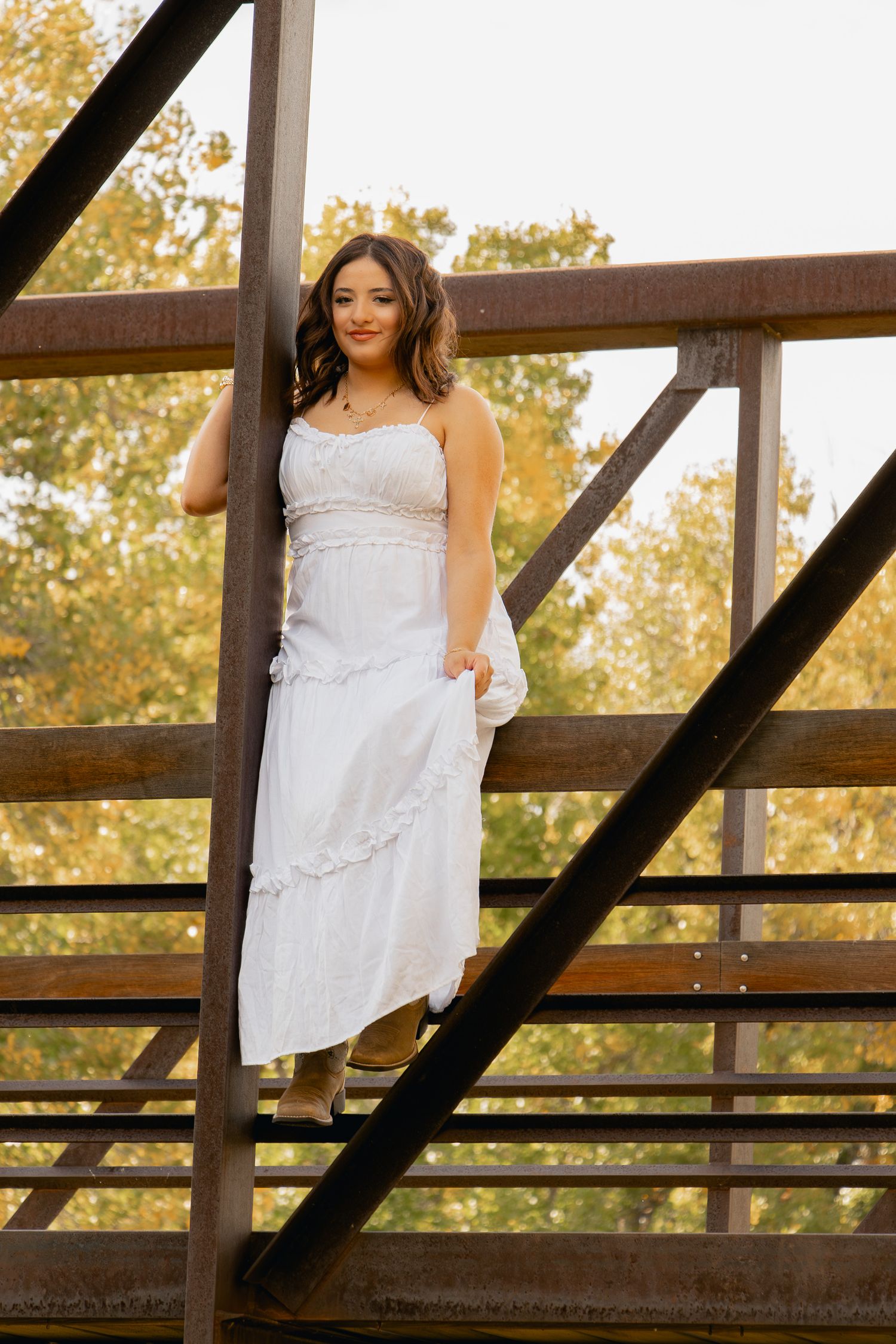 A white lace sundress photographed against a rustic wooden bridge railing during golden hour.