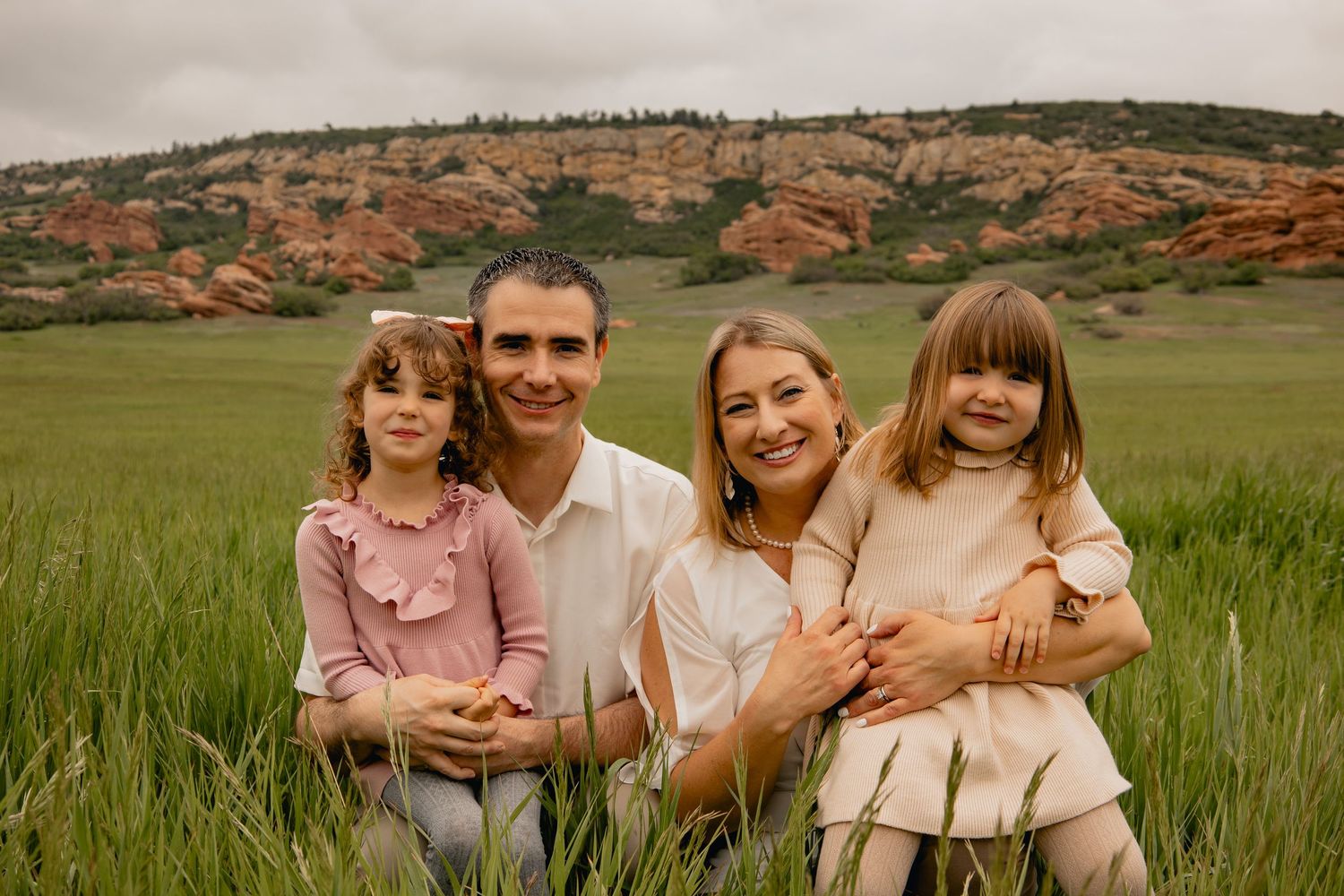 A group sits together in a green meadow with red rock formations visible on the hill in the background.
