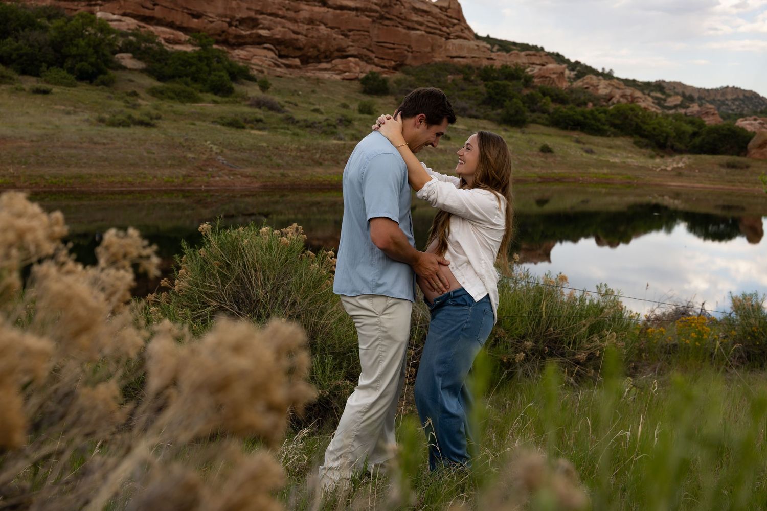 Couple embracing romantically in a scenic Colorado landscape with red rock formations and a reflective pond.