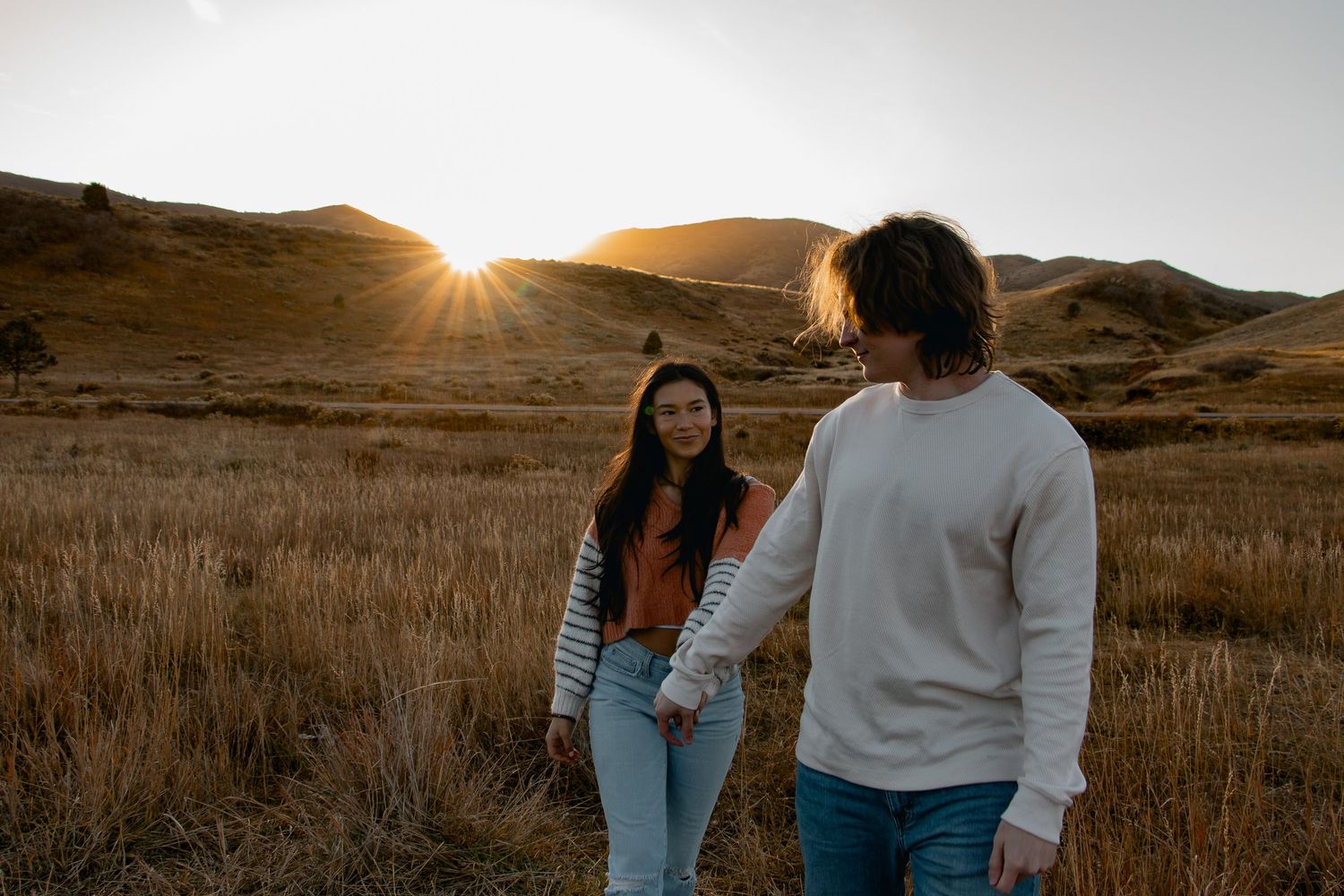 Couple embraces in golden sunset light on a hilltop with mountains in background.