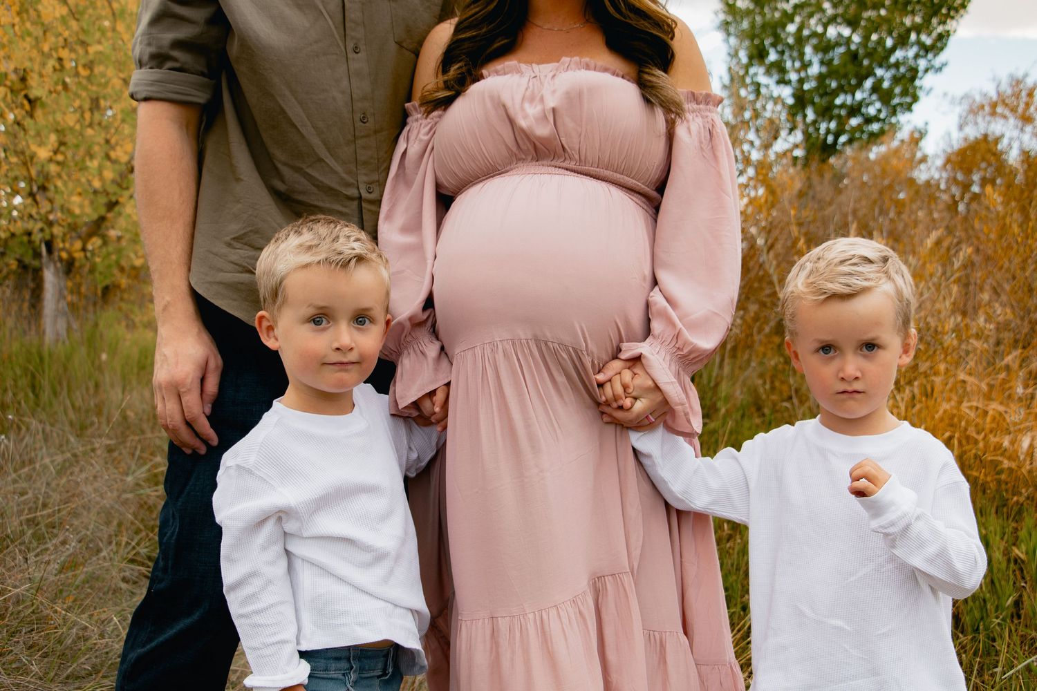 A family wearing coordinated pink and white outfits poses together during an autumn photo session in a park.