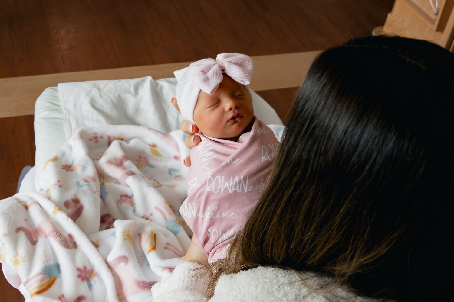 A baby wearing pink pajamas rests peacefully in a white crib with plush toys and soft bedding.