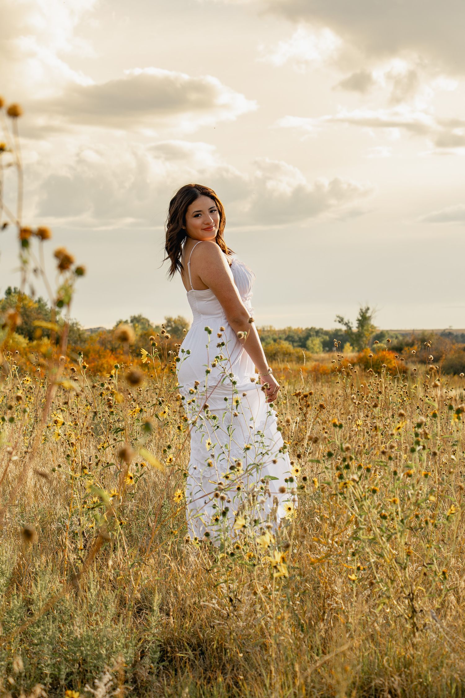 A person in a flowing white dress walks through a golden wildflower meadow at sunset.