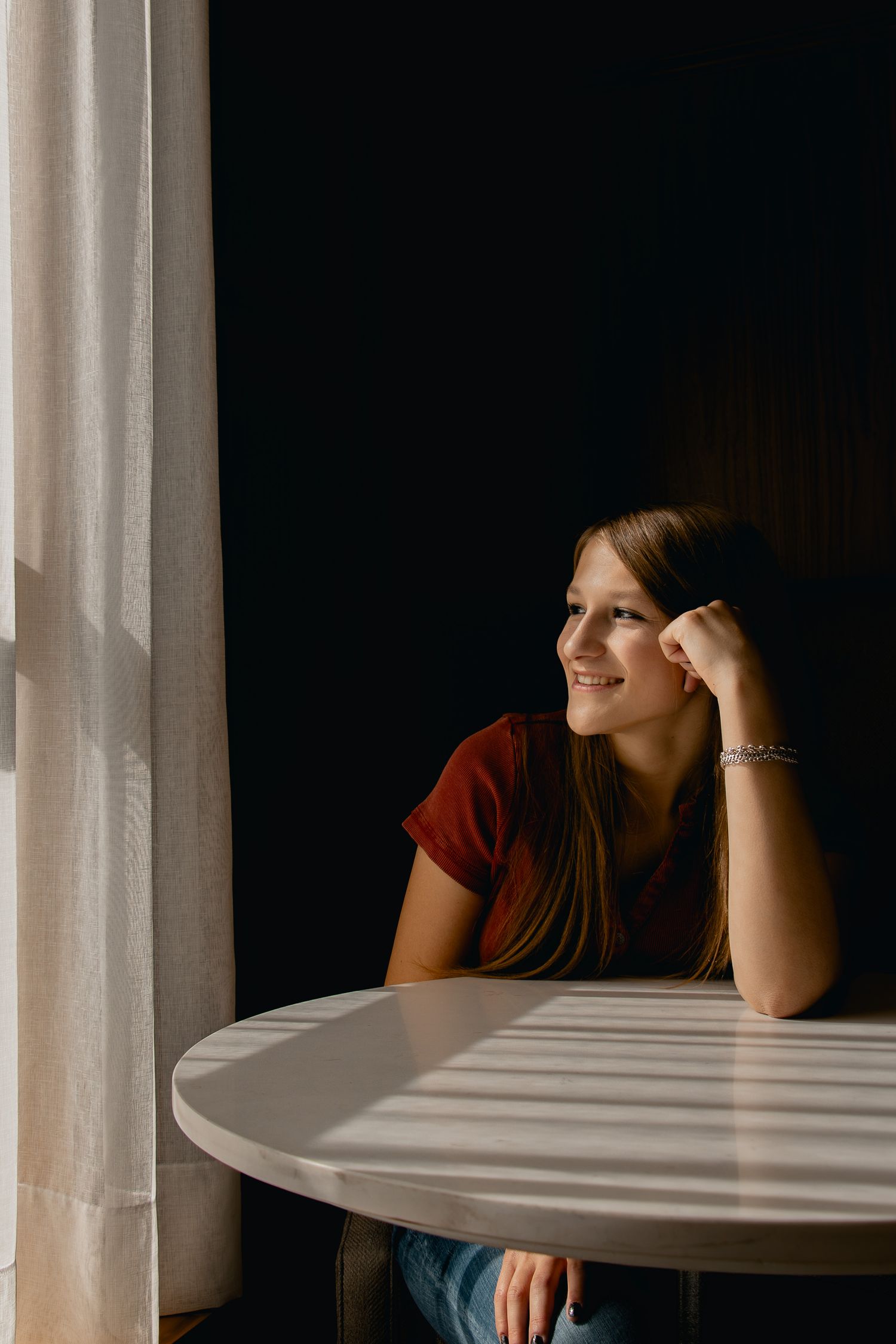 A person in a red shirt sits at a white round table near a window with dramatic natural lighting.