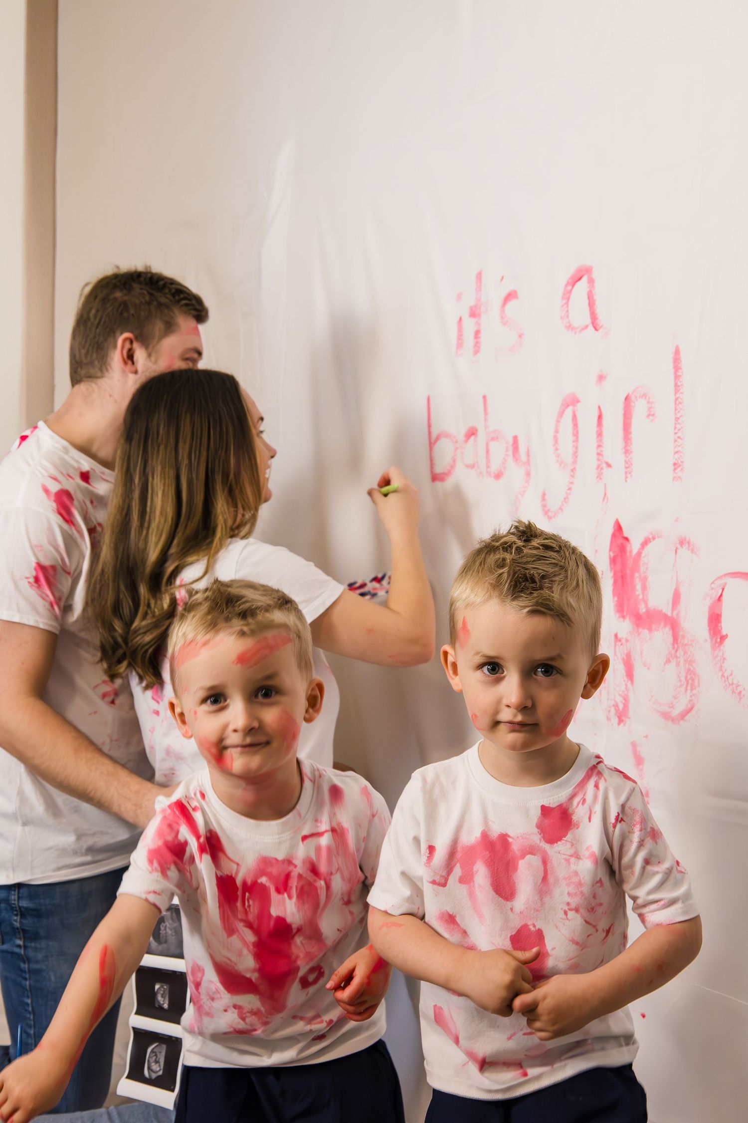 A sequence of photos showing two toddlers in white shirts stained with pink paint while playing indoors.