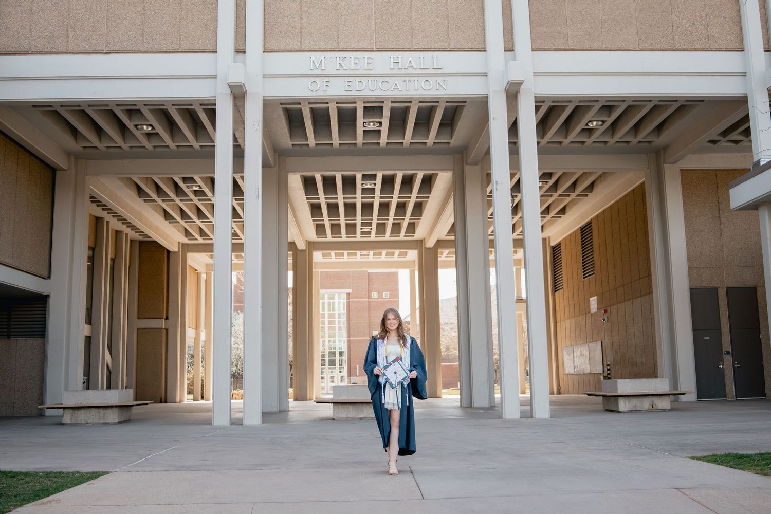 Student with backpack walks through modern university campus colonnade with white columns and beige walls.