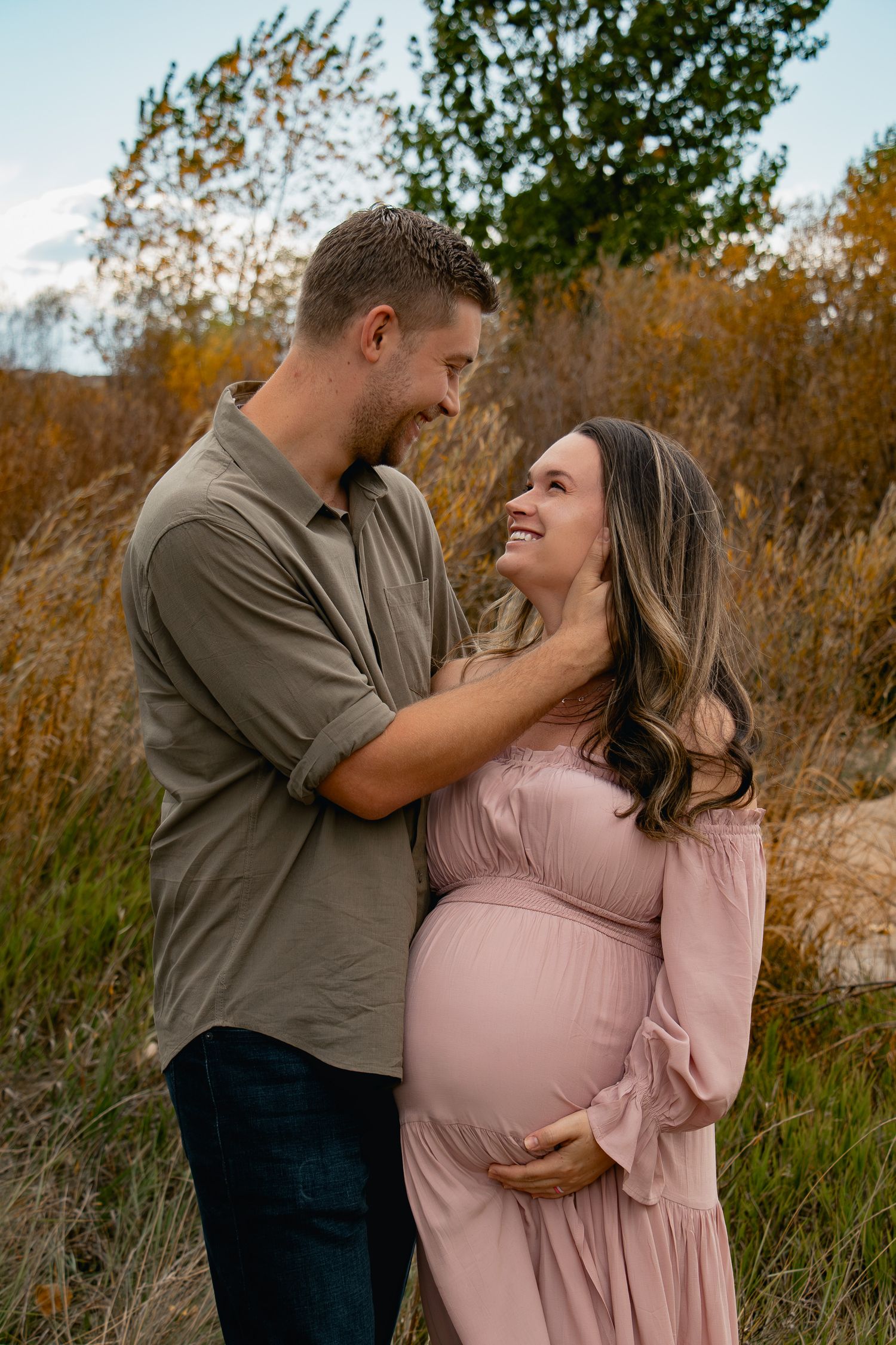 Couple shares tender moments in autumn field with woman wearing pink dress and man in olive shirt.