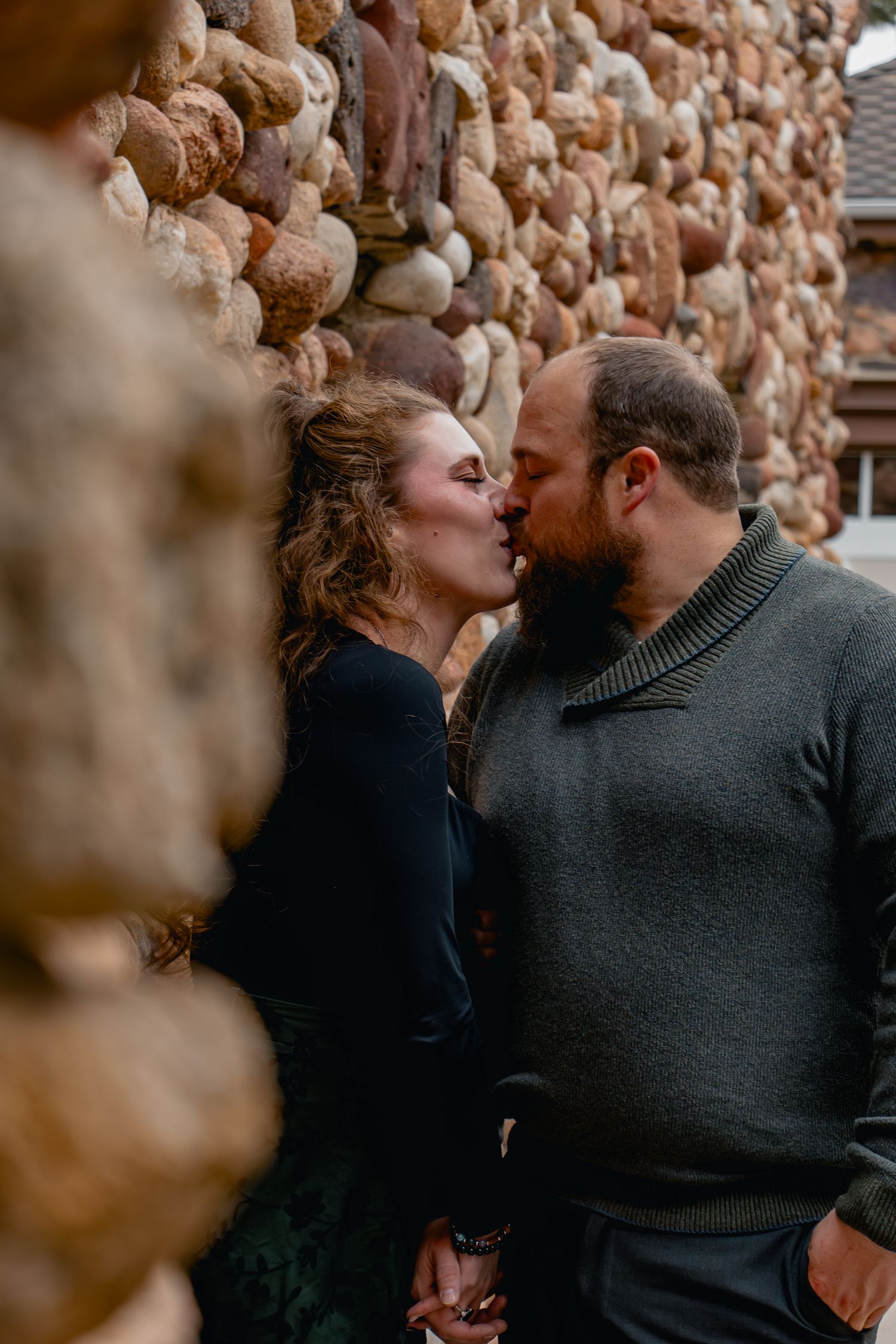 A romantic moment shared between a couple against a rustic stone wall background.