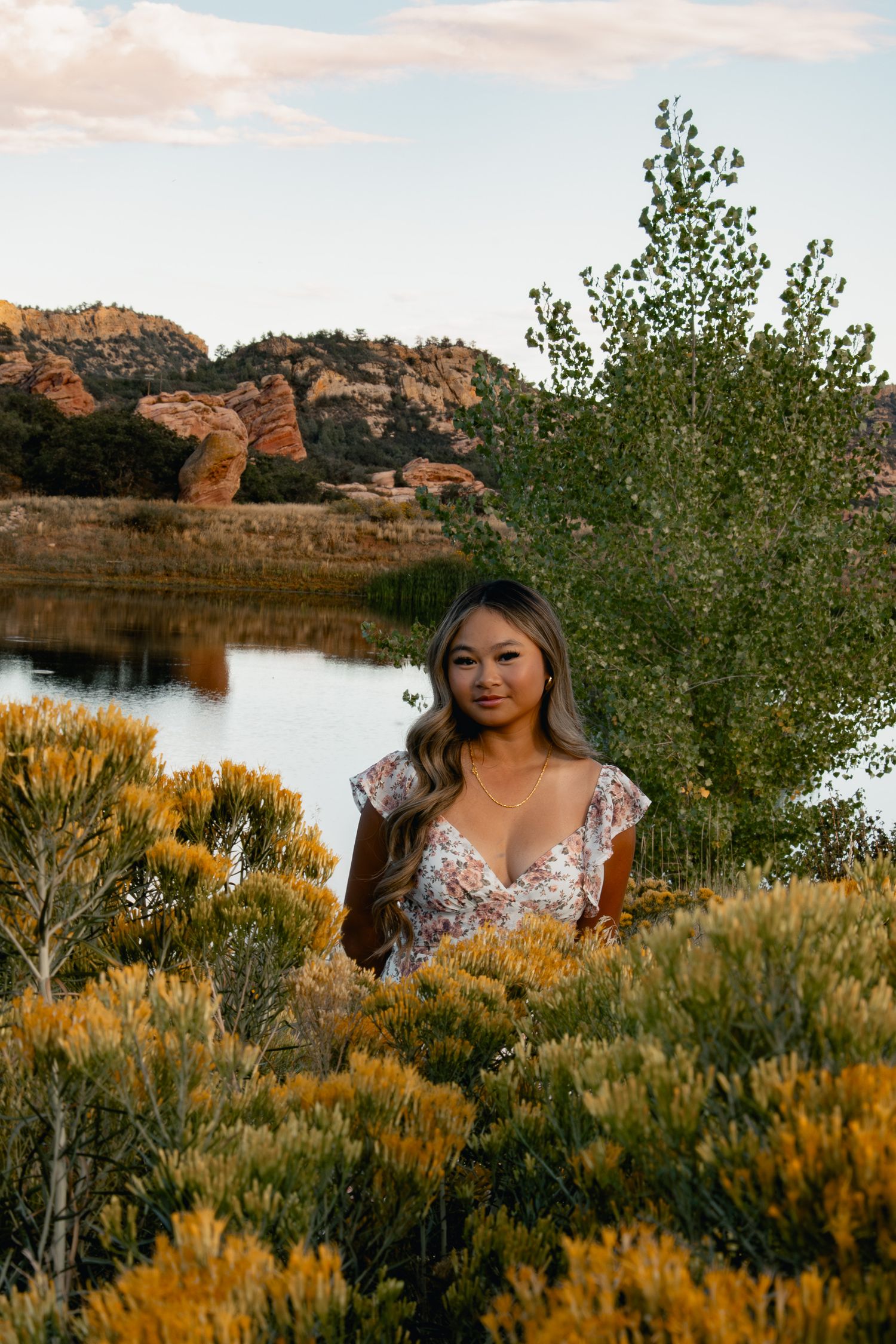 Golden autumn foliage surrounds a tranquil lake scene with red rock formations in the background at sunset.
