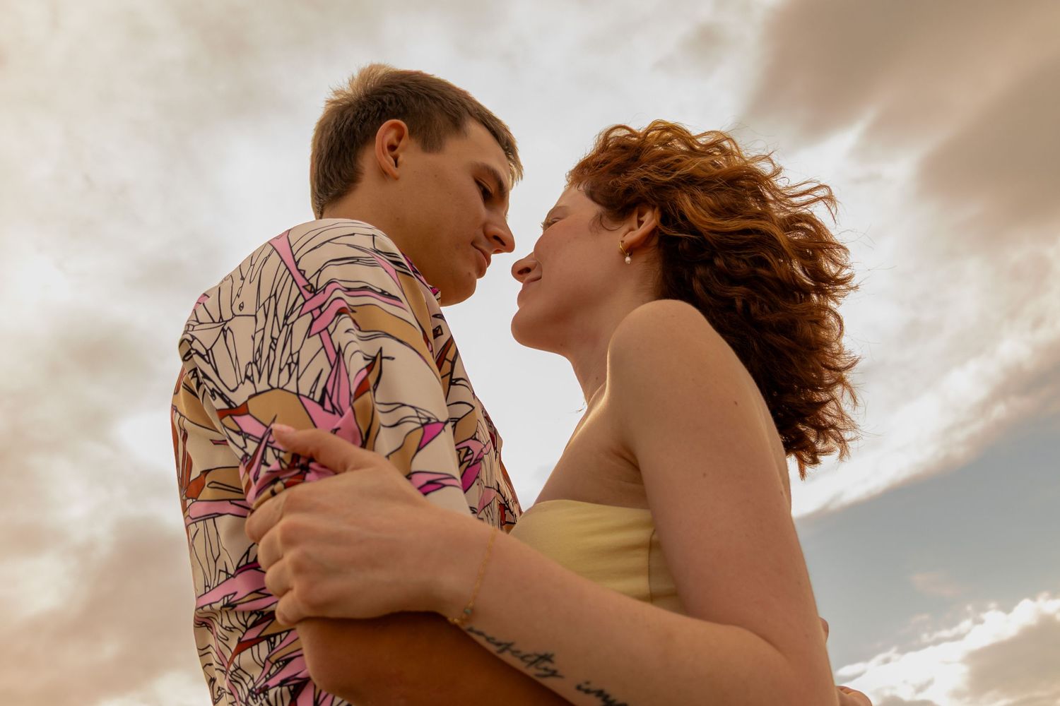 A couple embraces intimately under dramatic cloudy skies during a romantic sunset moment.