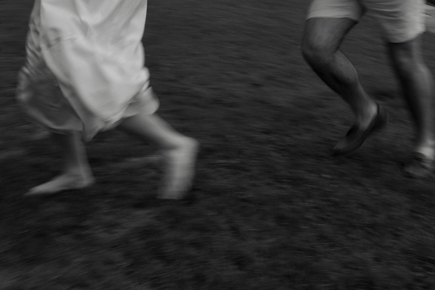 Black and white motion blur photo of couple running on grass, capturing movement and energy.