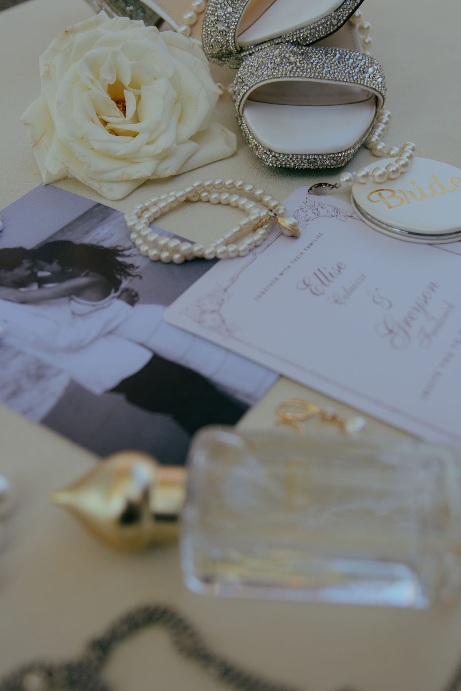 Wedding details including white roses, pearls, and elegant stationery arranged on a light surface.