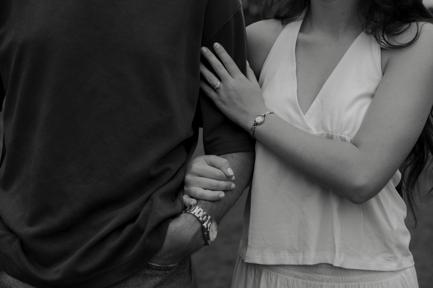 Black and white photo of a couple holding hands, woman in white dress wearing a bracelet and ring.
