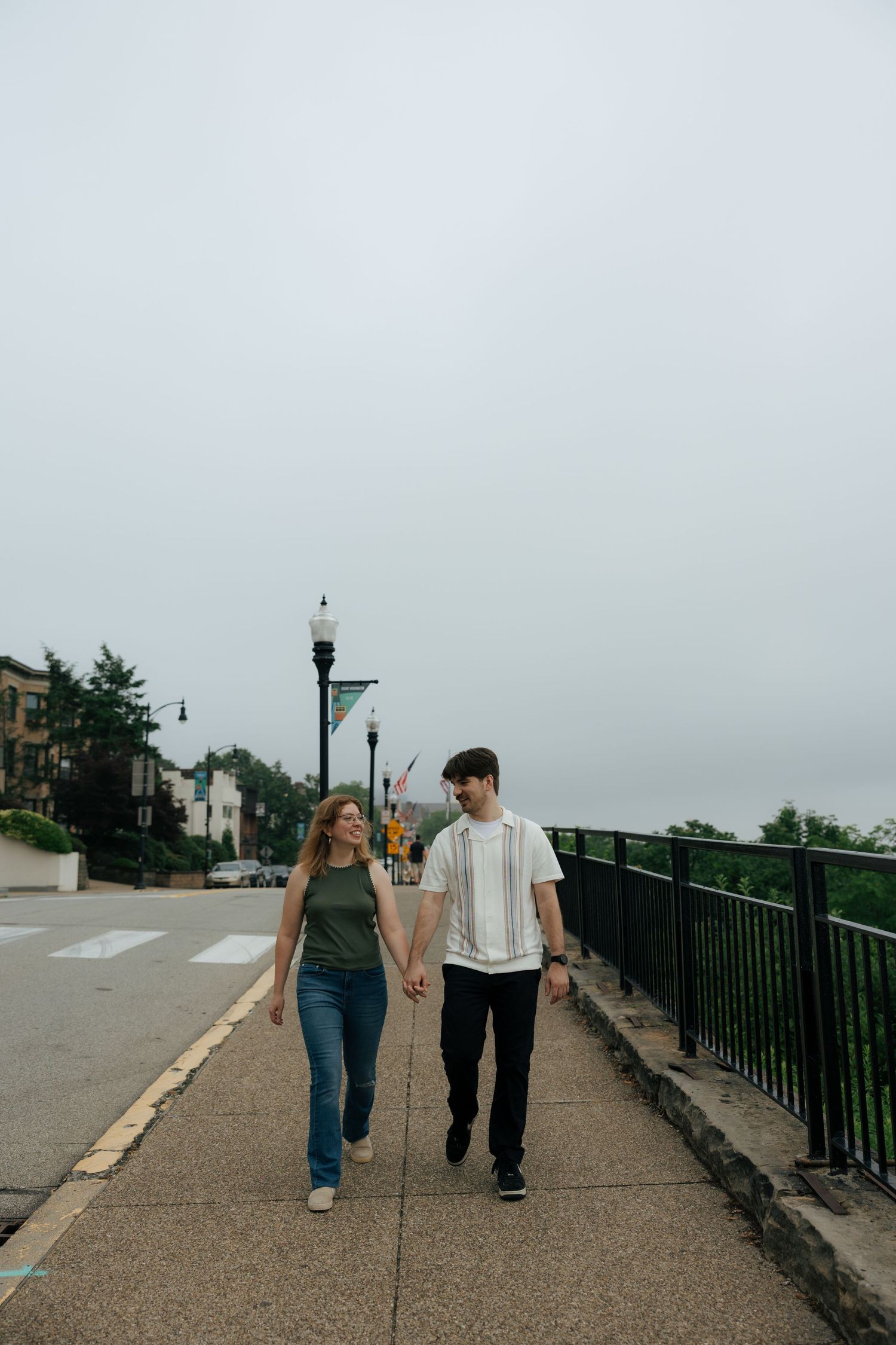 Couple holding hands and walking together on a city sidewalk on a cloudy day.