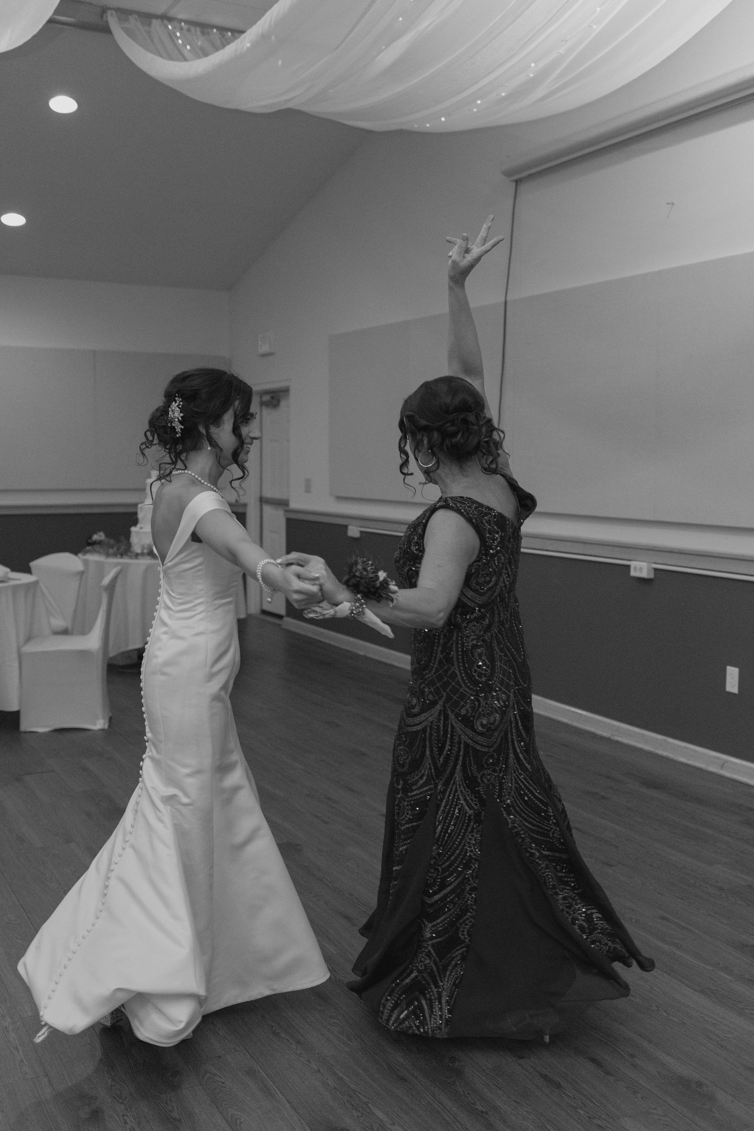Black and white photo of bride and mother sharing a joyful dance together at wedding reception.