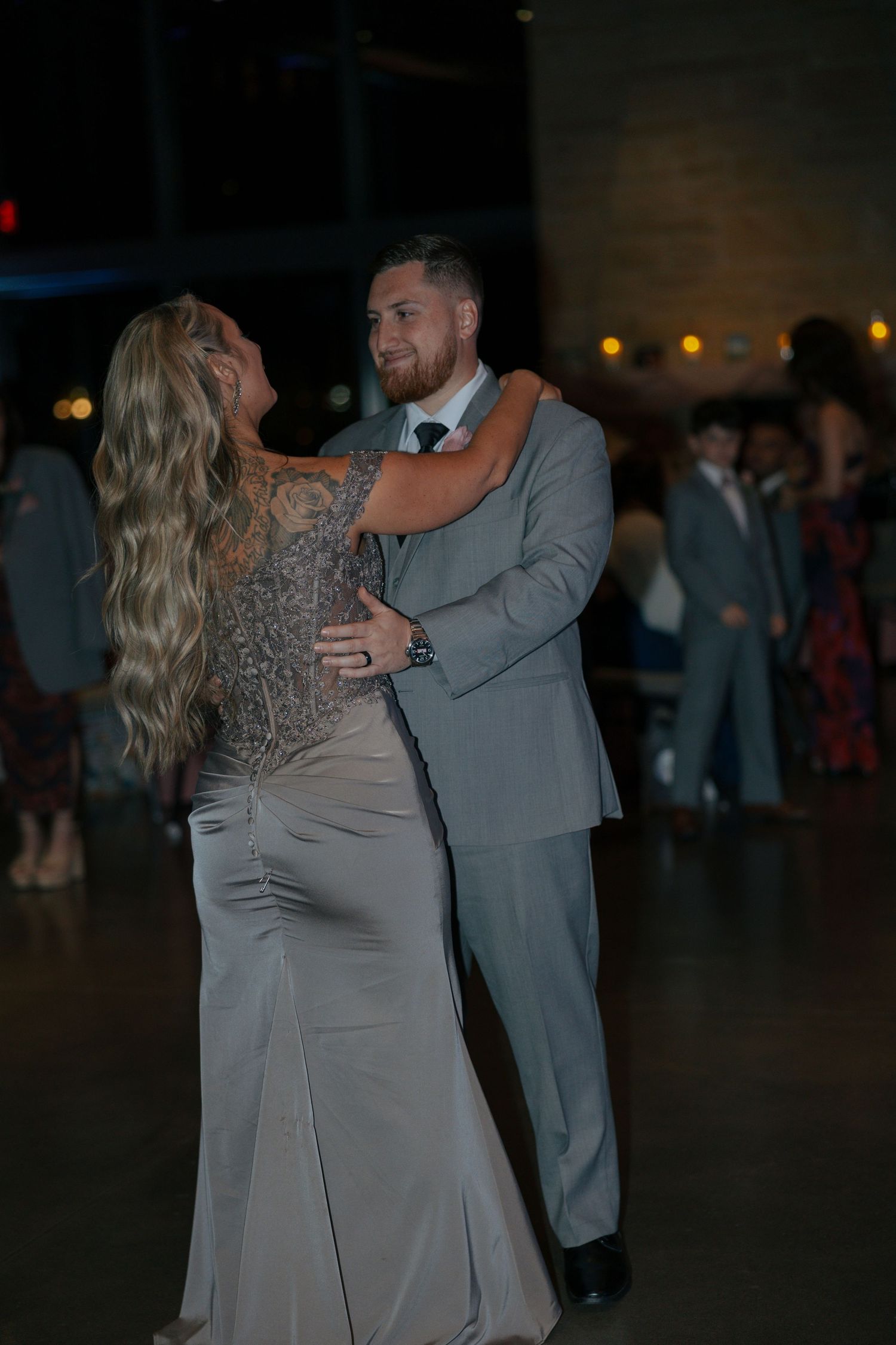 Couple sharing a romantic slow dance at a wedding reception, man in gray suit, woman in elegant gray gown with lace back.