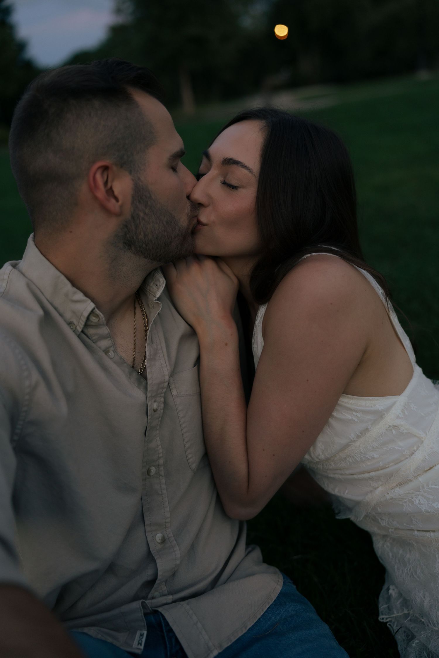 Couple sharing a romantic kiss outdoors on grass during twilight evening light.