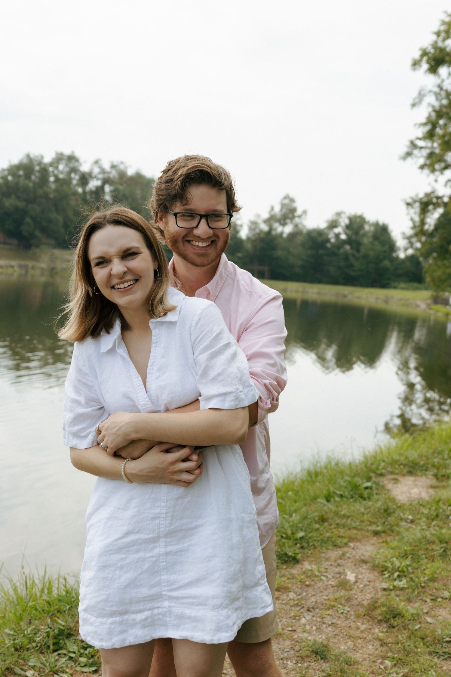 A couple shares an intimate embrace by a serene lake on a sunny summer afternoon.