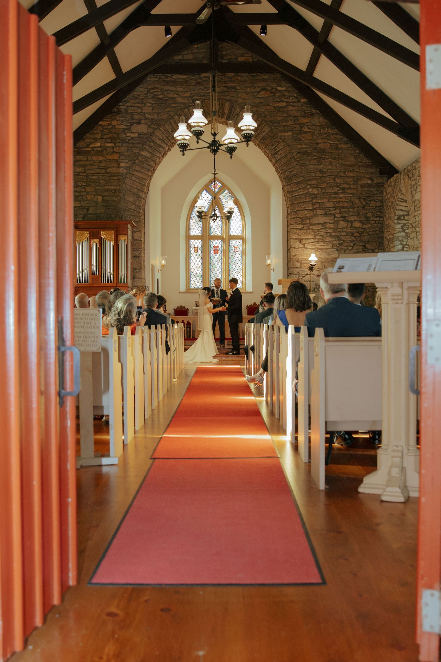 Elegant stone chapel interior with red carpet aisle and arched stained glass window.