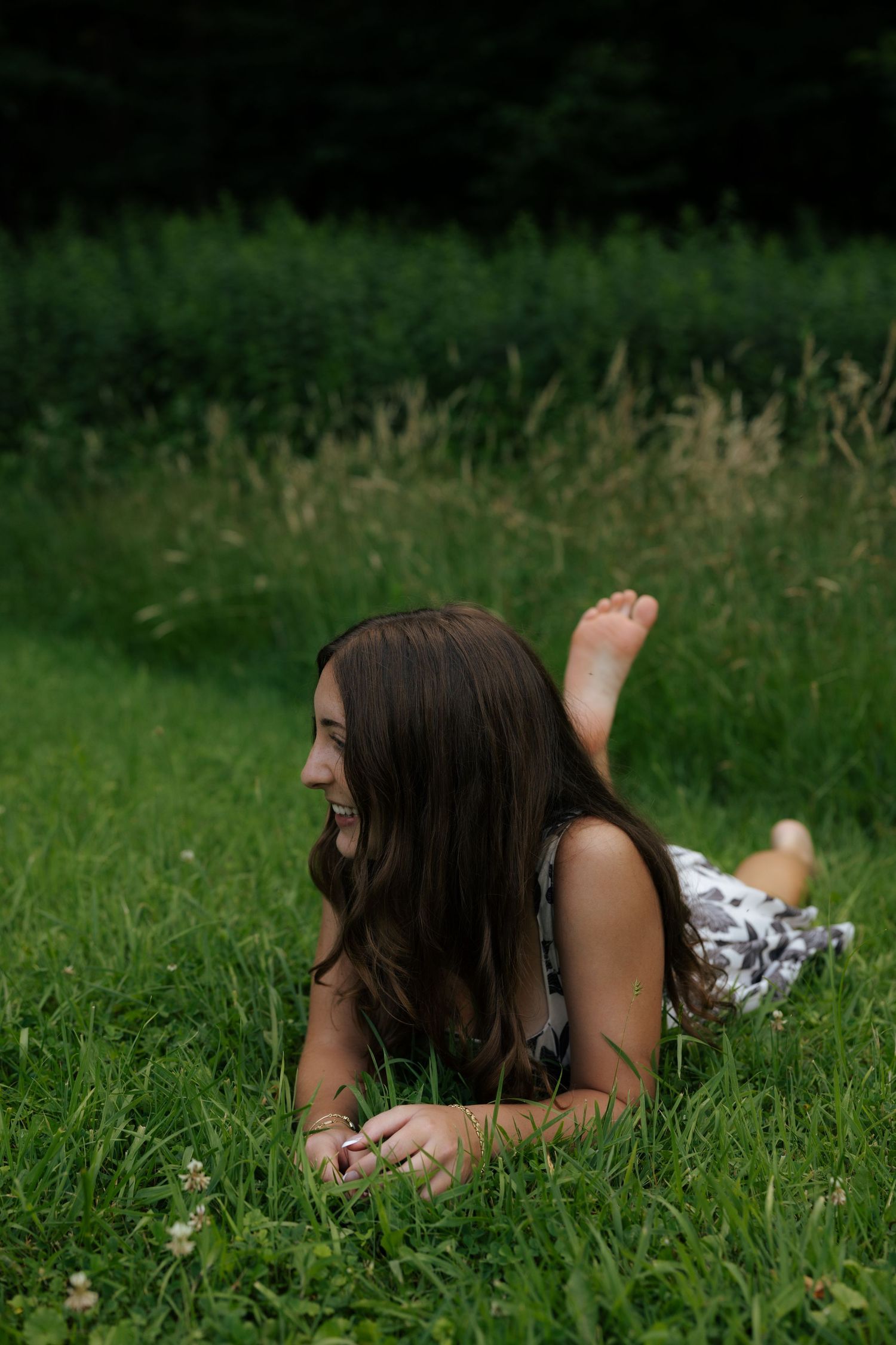 Laughing young woman lying barefoot in lush green grass outdoors.