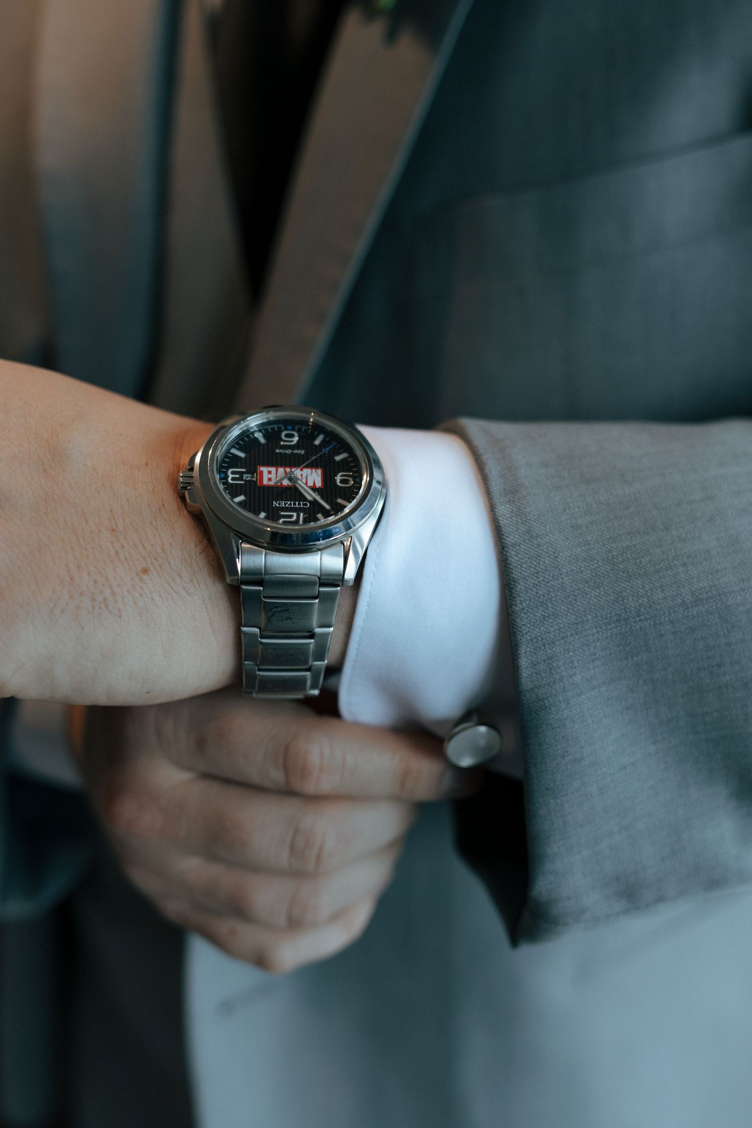 Man in gray suit checking silver analog wristwatch with black dial and date display on his wrist.