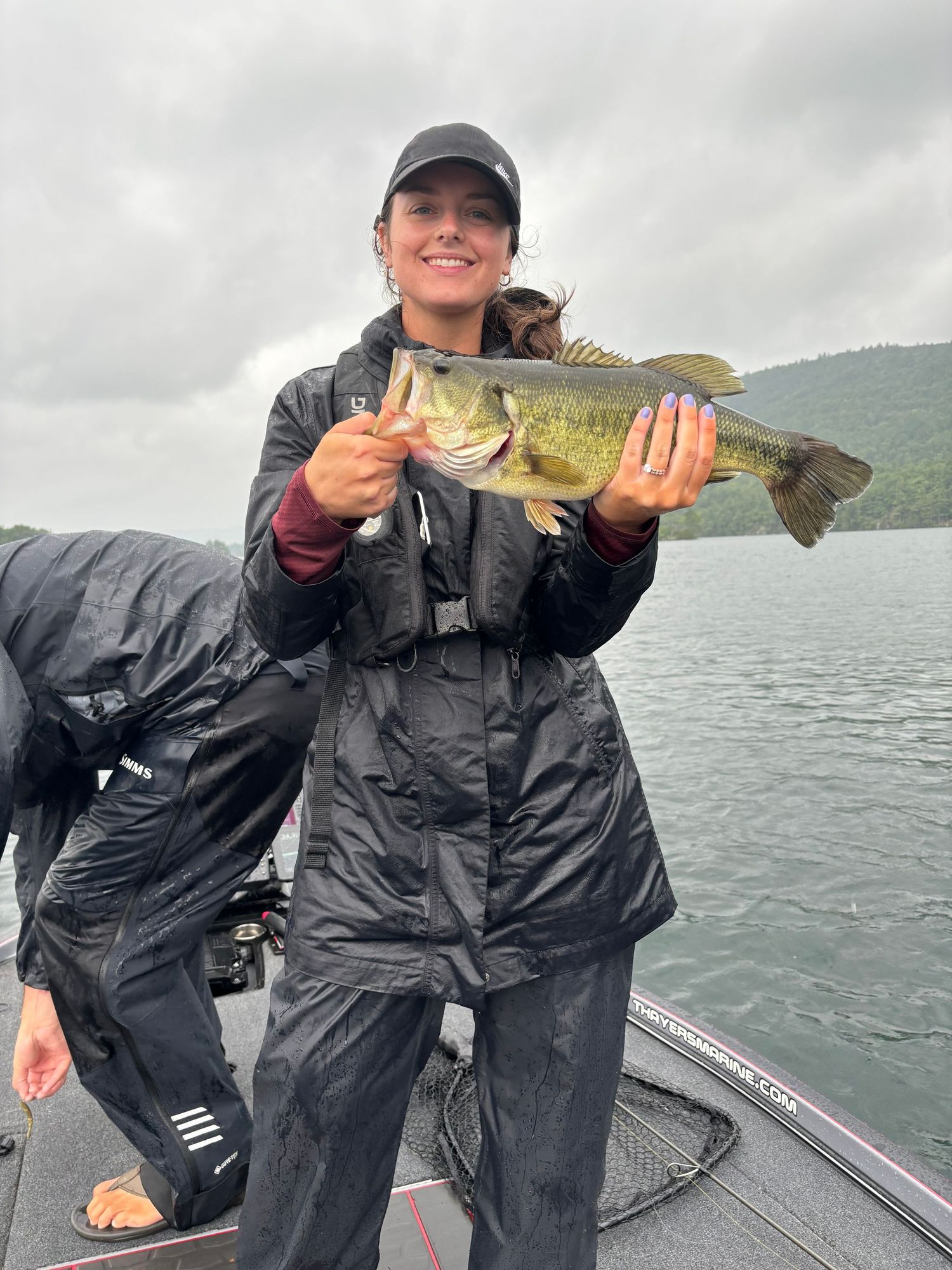 Angler in rain gear proudly displays large bass caught on overcast day on the lake.