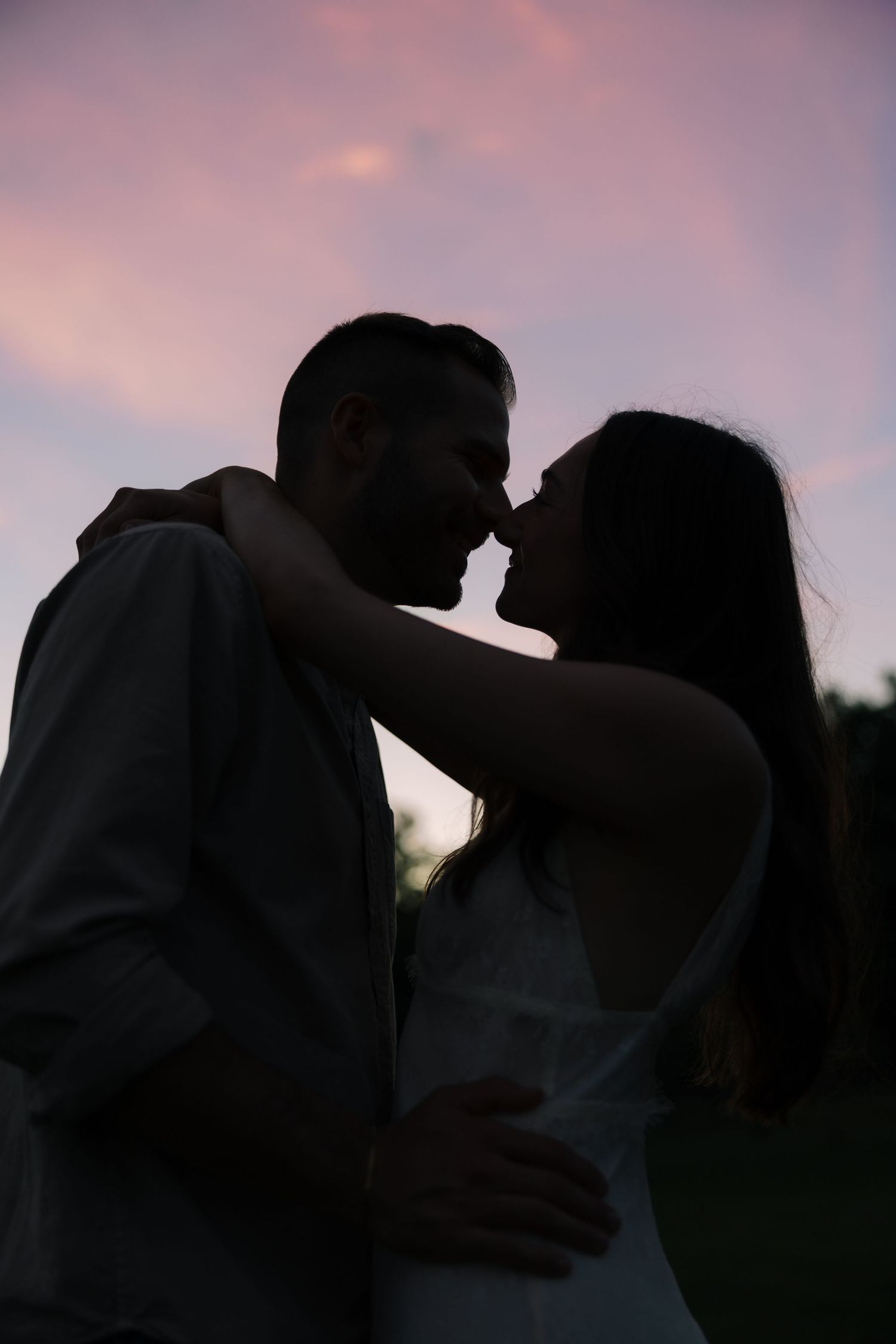 Silhouette of a couple about to kiss against a stunning pink and purple sunset sky.